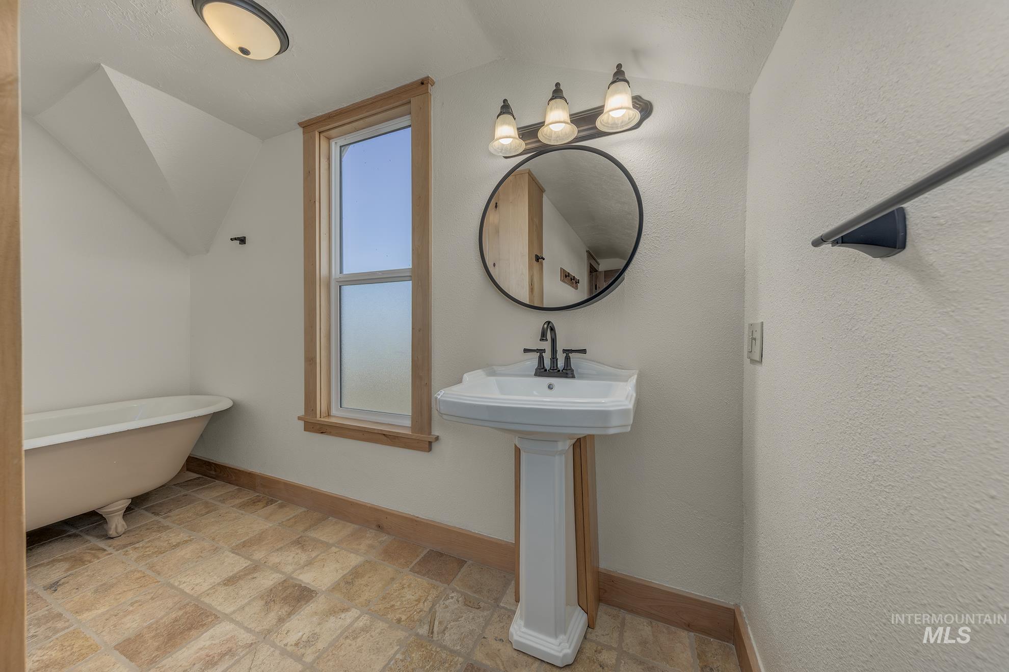 Bathroom featuring stone tile floors, a freestanding tub, vaulted ceiling, and a textured wall