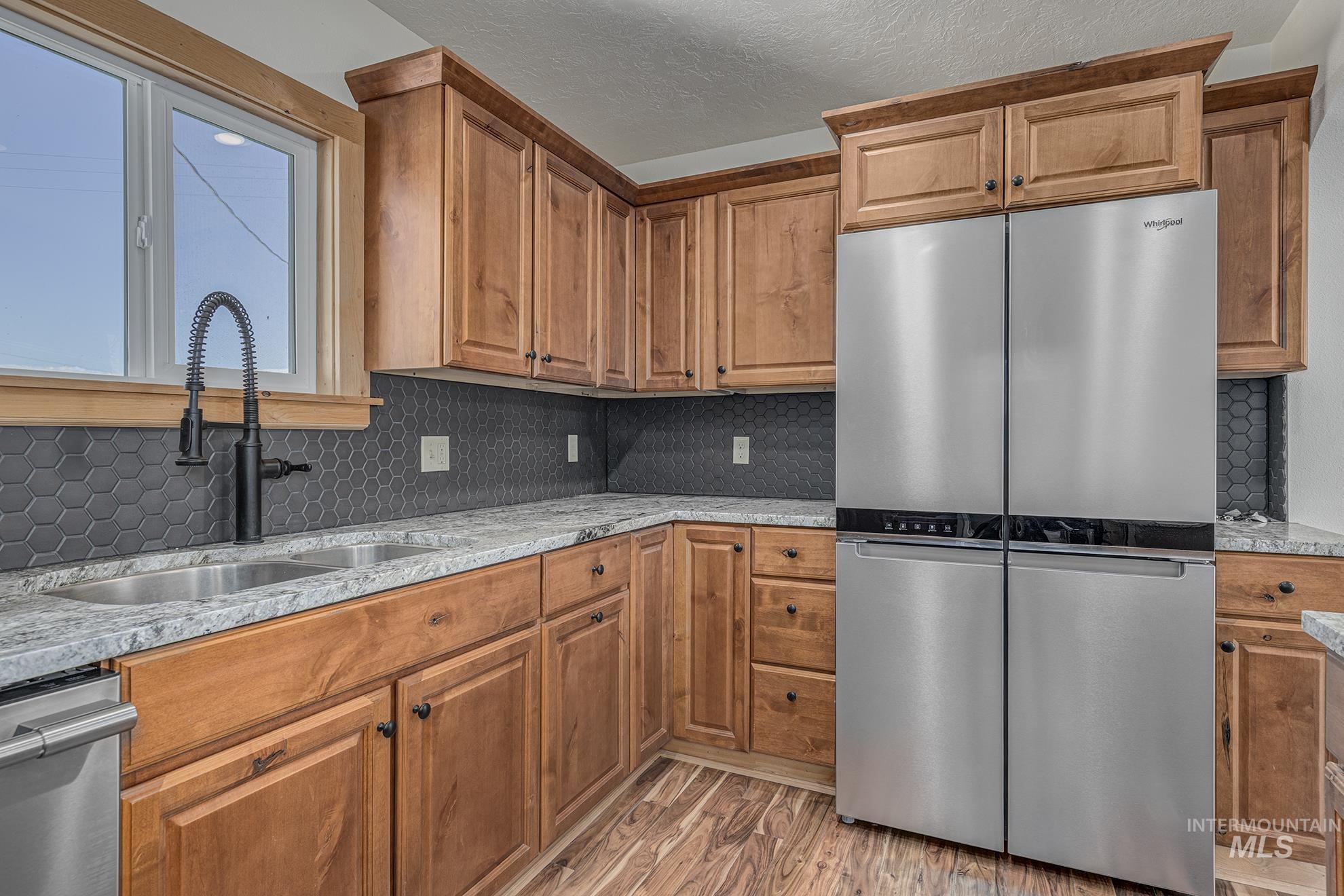 Kitchen with appliances with stainless steel finishes, decorative backsplash, light stone countertops, light wood-style flooring, and brown cabinetry