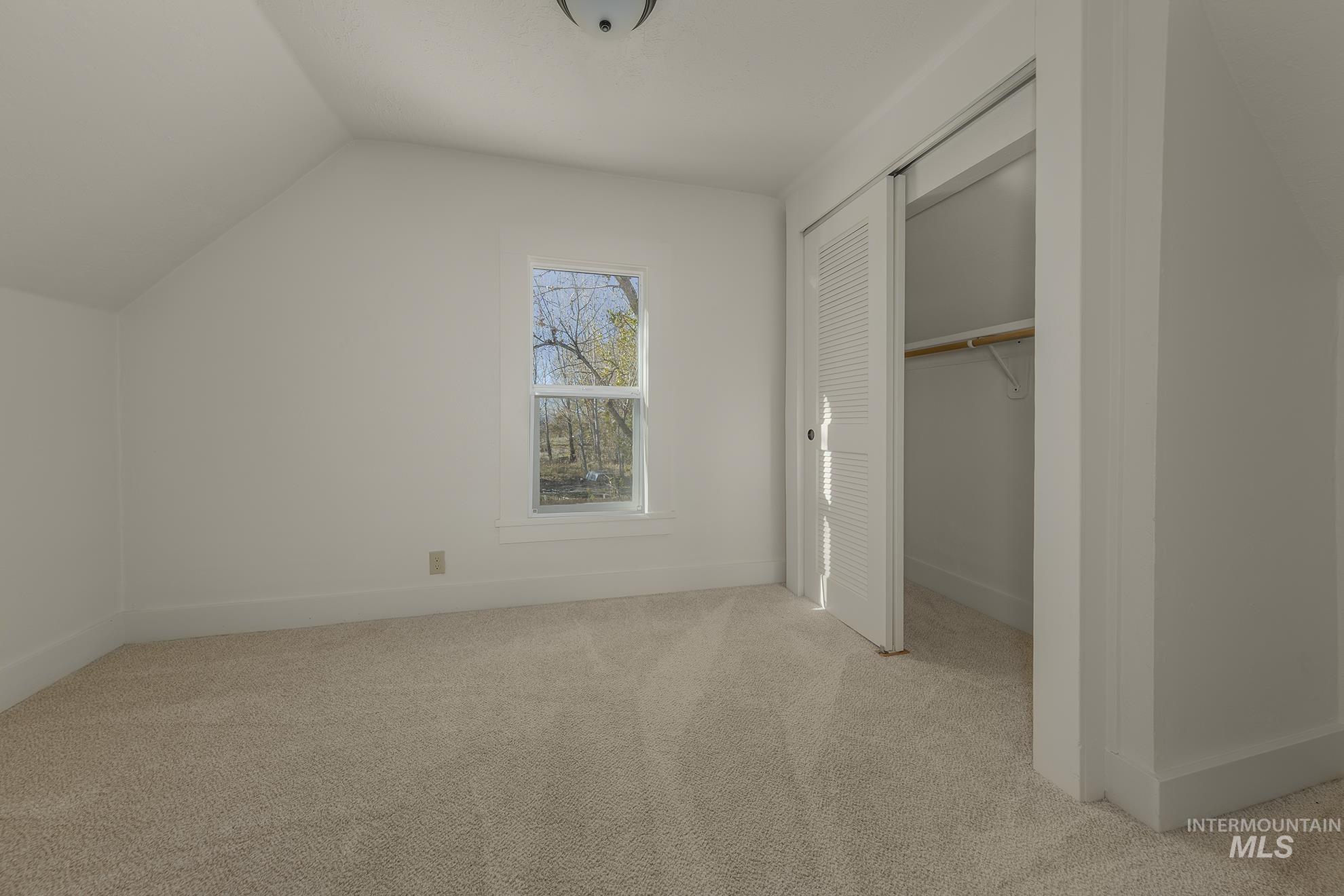 Unfurnished bedroom with light colored carpet, a closet, and lofted ceiling