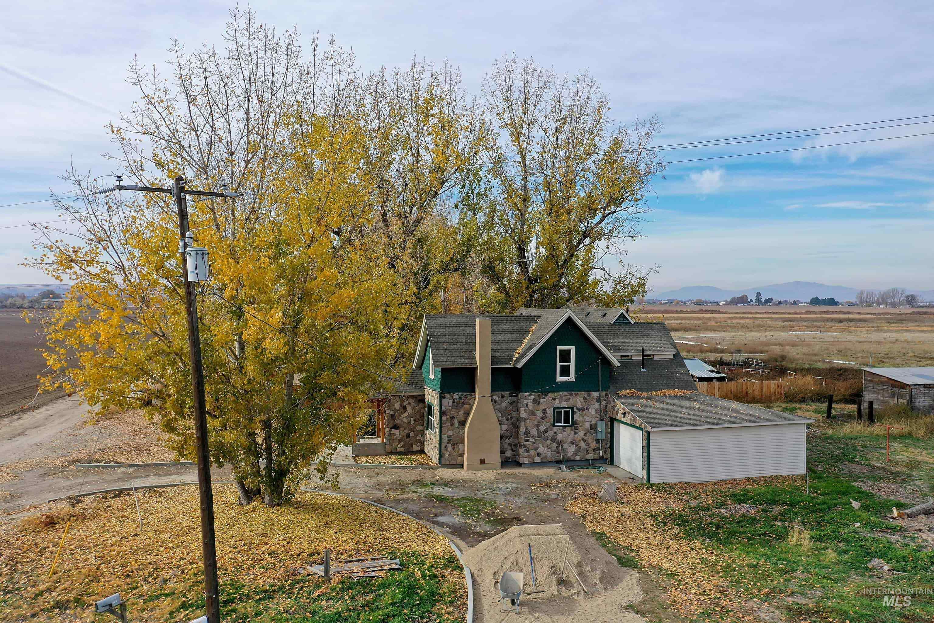 View of front facade featuring a view of countryside, stone siding, a shingled roof, driveway, and a garage
