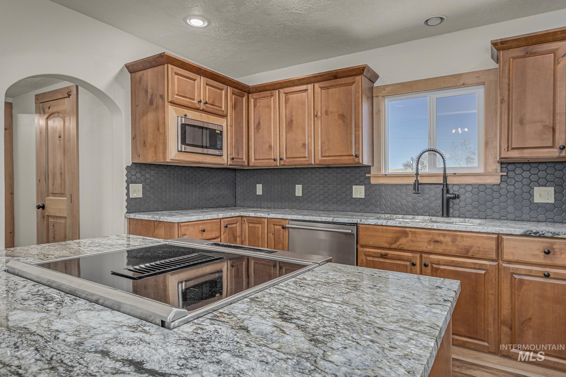 Kitchen with tasteful backsplash, stainless steel appliances, brown cabinetry, a textured ceiling, and recessed lighting