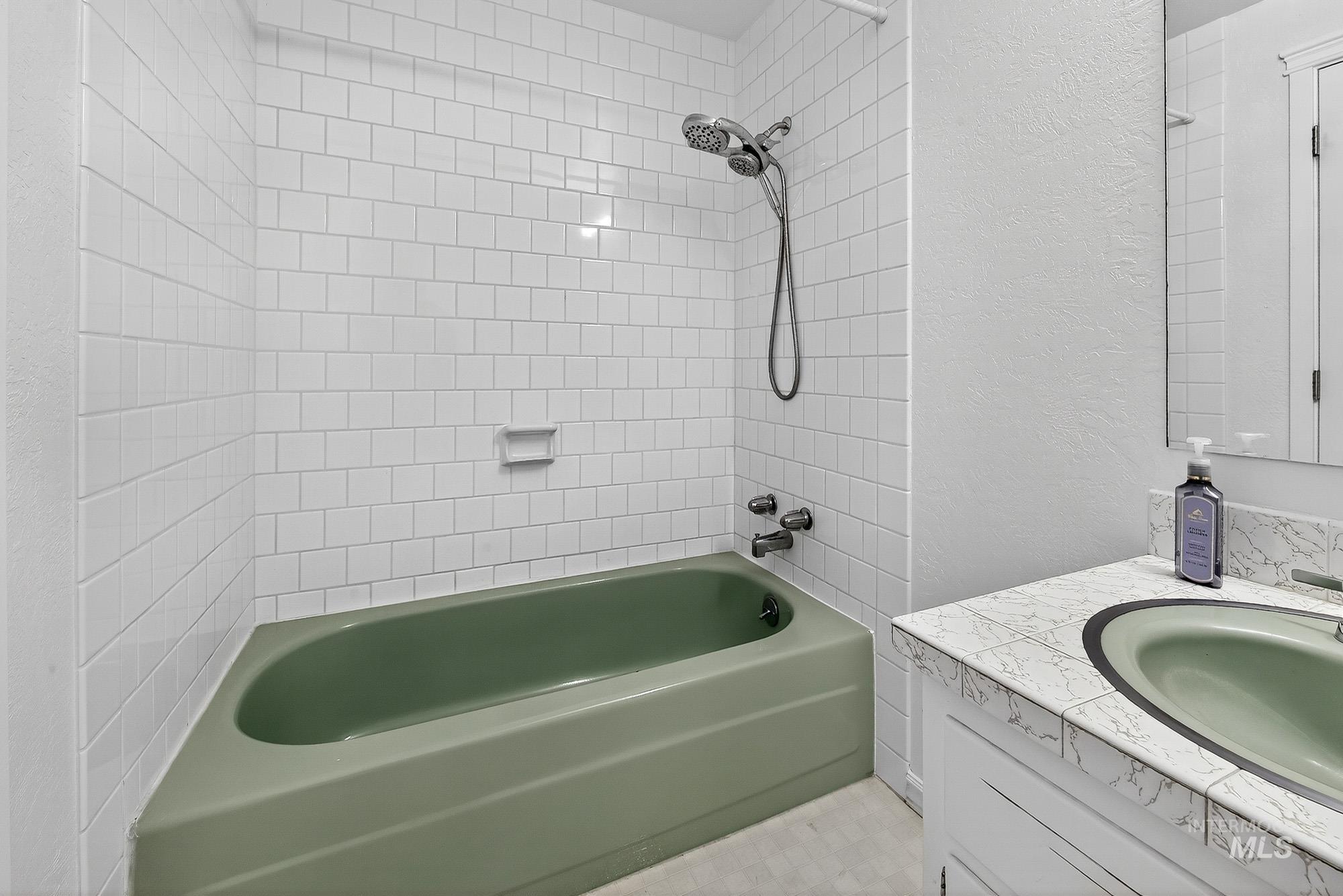 Bathroom featuring a textured wall, shower / tub combination, and vanity