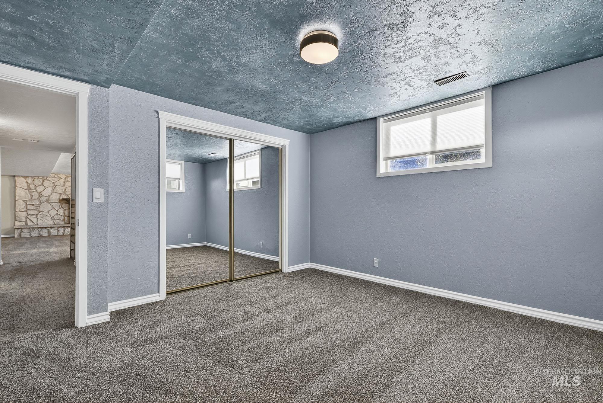 Unfurnished bedroom featuring carpet flooring, multiple windows, a textured ceiling, a closet, and a textured wall
