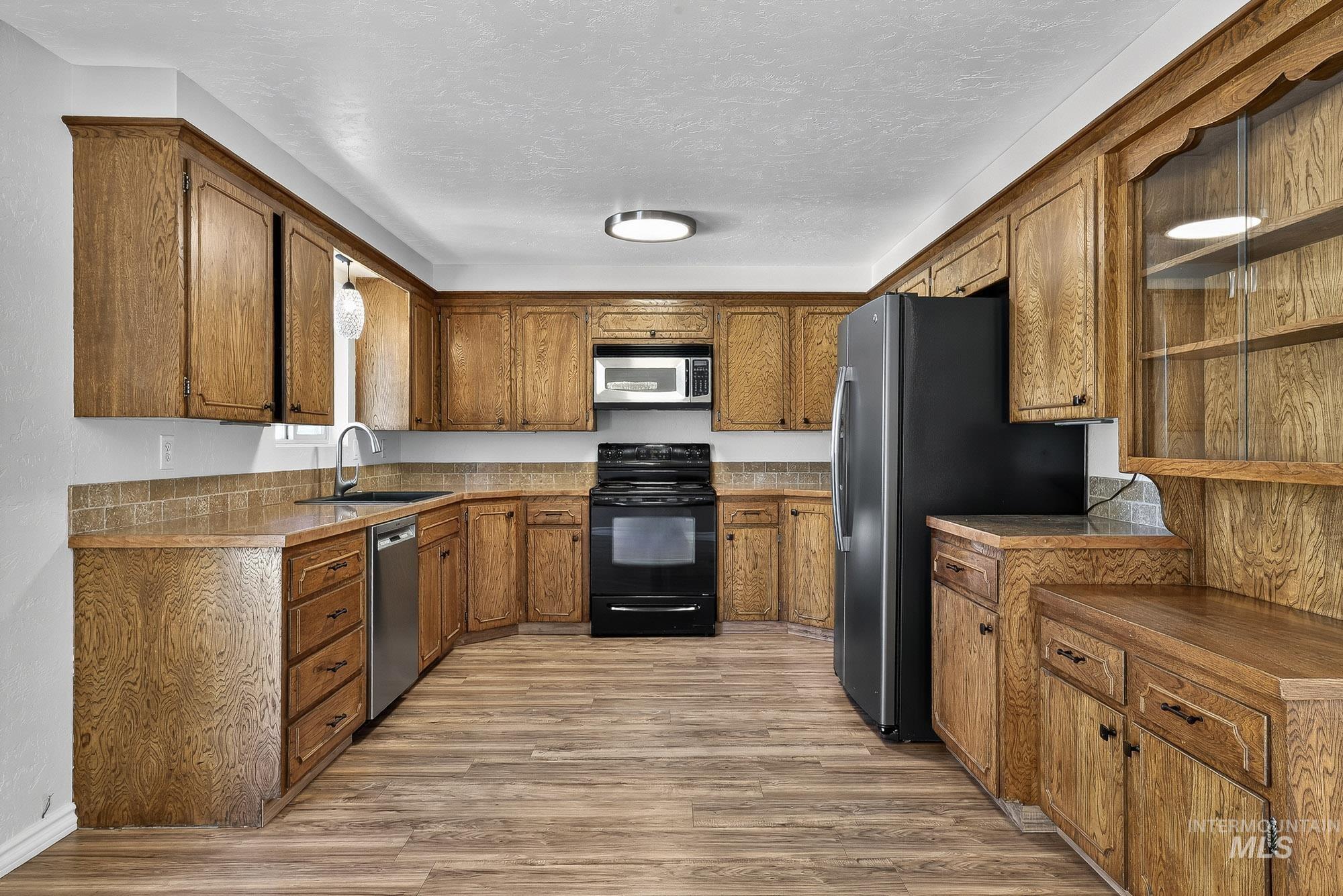 Kitchen with brown cabinetry, stainless steel appliances, light wood finished floors, and a textured ceiling