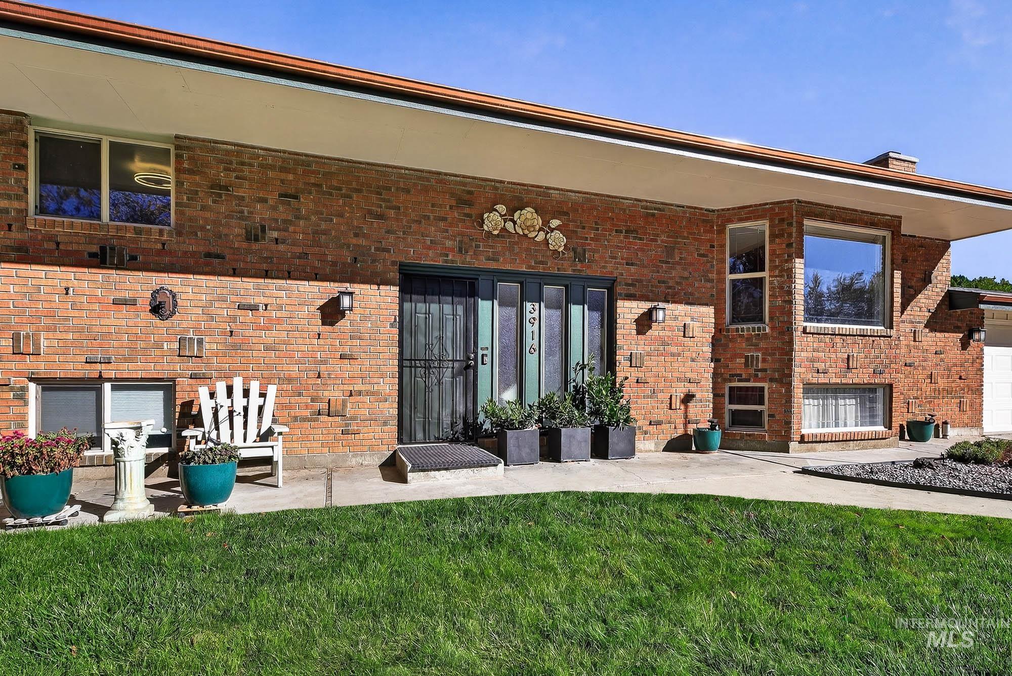 View of exterior entry with brick siding, a patio, and a yard