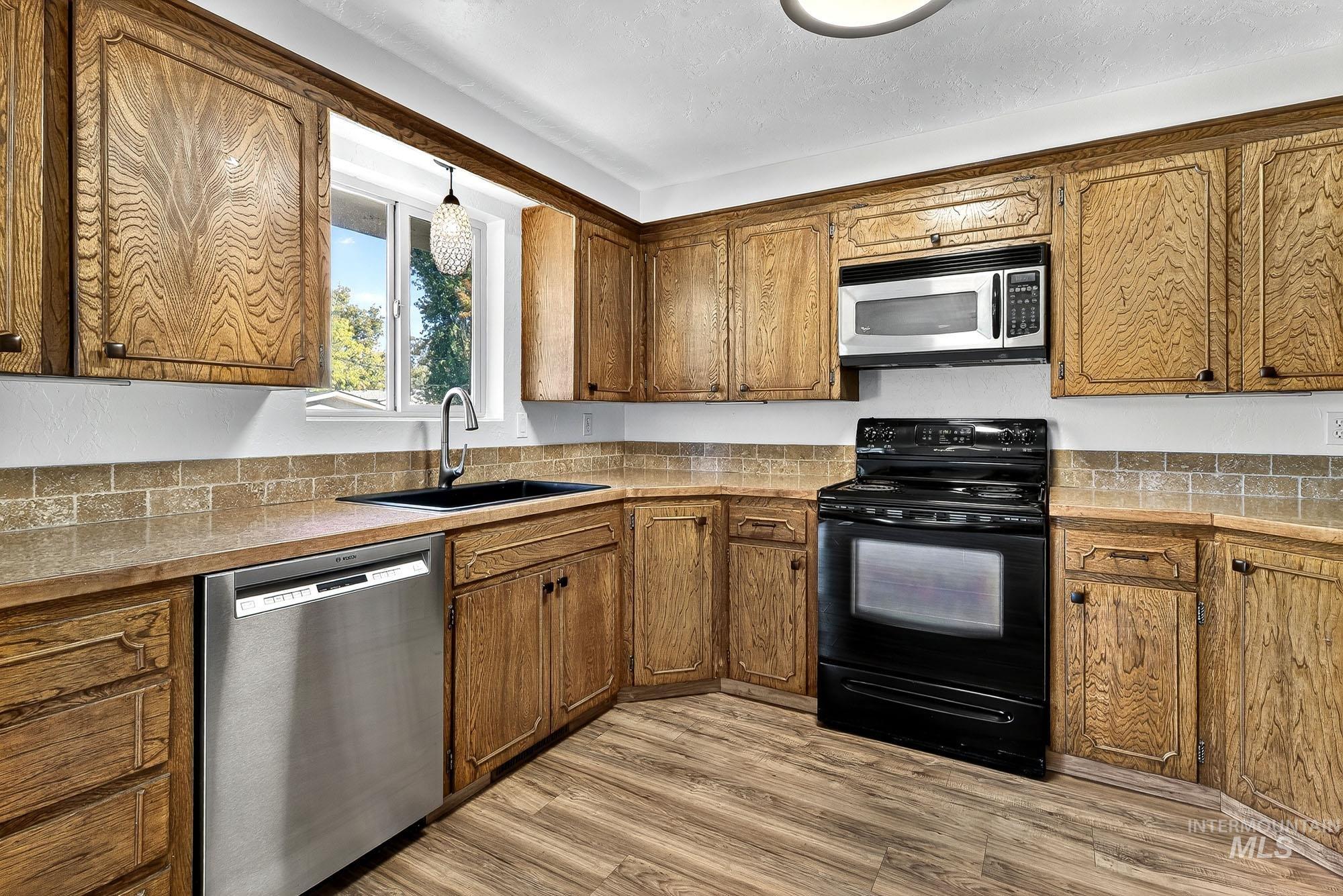Kitchen featuring stainless steel appliances, decorative light fixtures, light wood-style flooring, and brown cabinetry