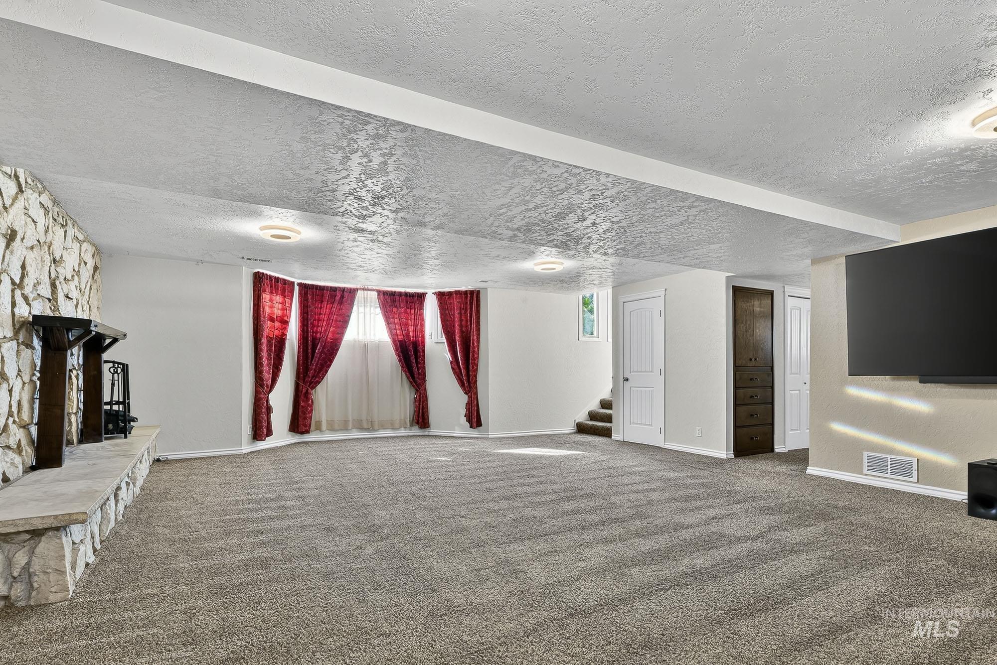 Unfurnished living room with carpet flooring, a textured ceiling, stairway, and a fireplace