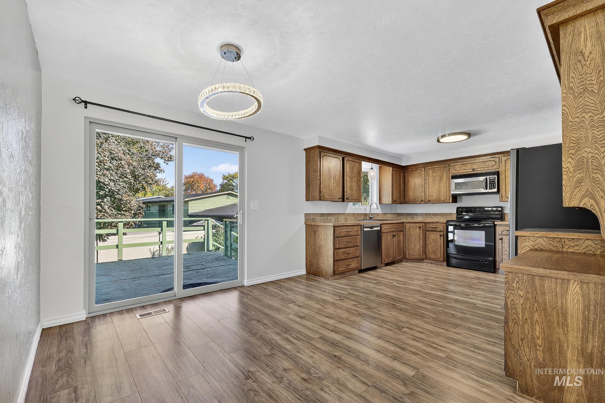 Kitchen with appliances with stainless steel finishes, dark wood-style floors, brown cabinetry, light countertops, and decorative light fixtures
