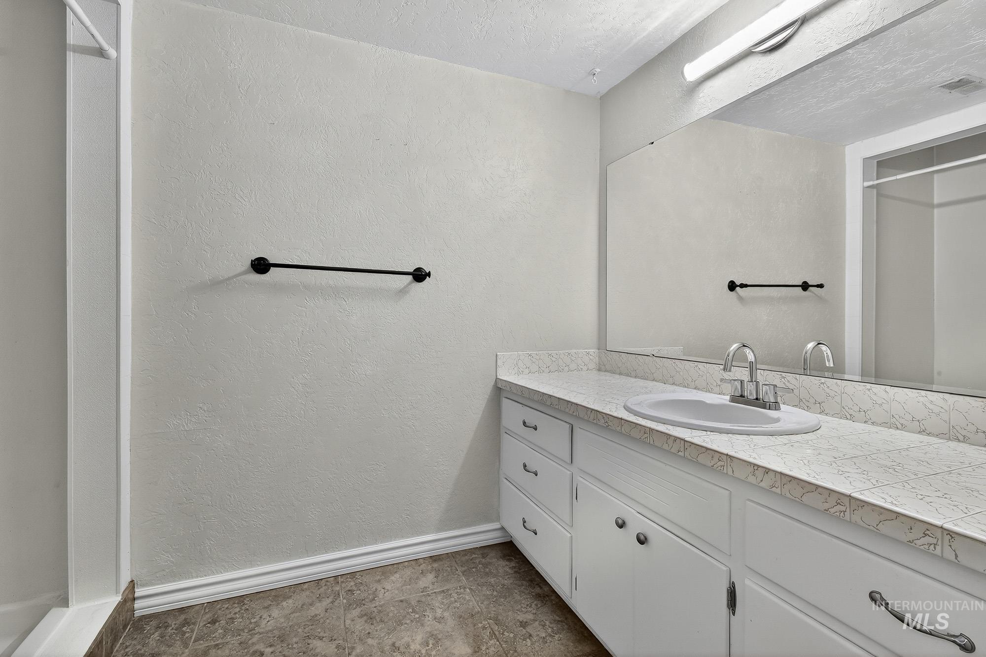 Full bath featuring a textured wall, vanity, a stall shower, and a textured ceiling