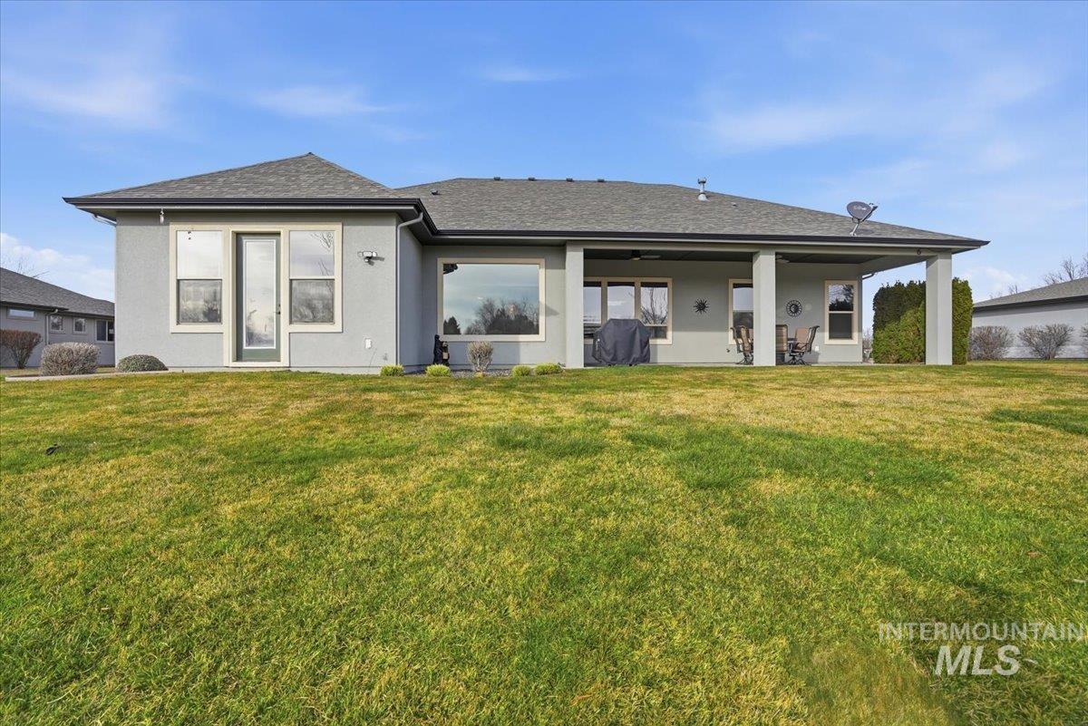 Rear view of property featuring a lawn, a patio area, and stucco siding