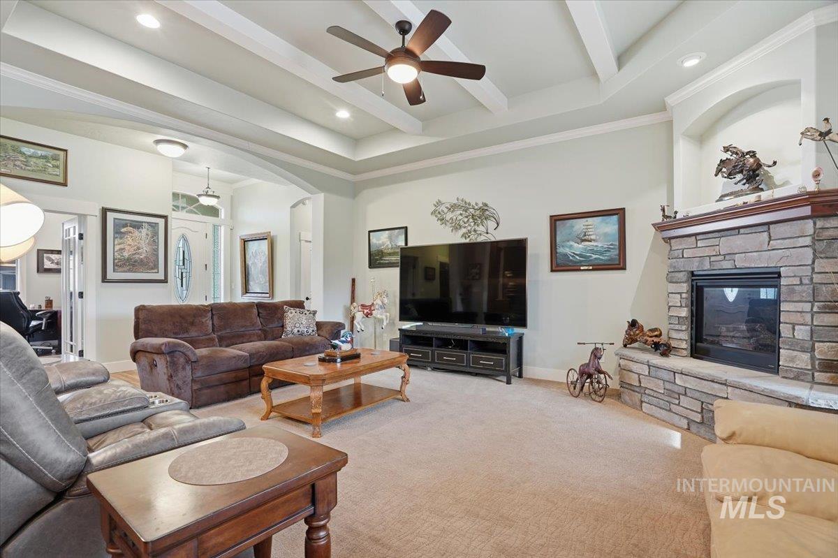 Carpeted living area with a stone fireplace, a ceiling fan, recessed lighting, arched walkways, and crown molding
