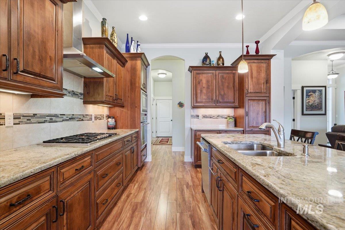 Kitchen with arched walkways, tasteful backsplash, light wood-type flooring, light stone countertops, and crown molding