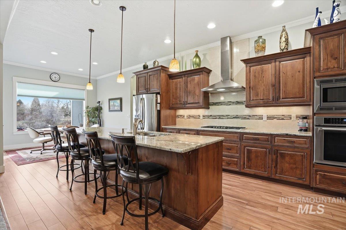 Kitchen featuring crown molding, stainless steel appliances, a kitchen breakfast bar, hanging light fixtures, and an island with sink