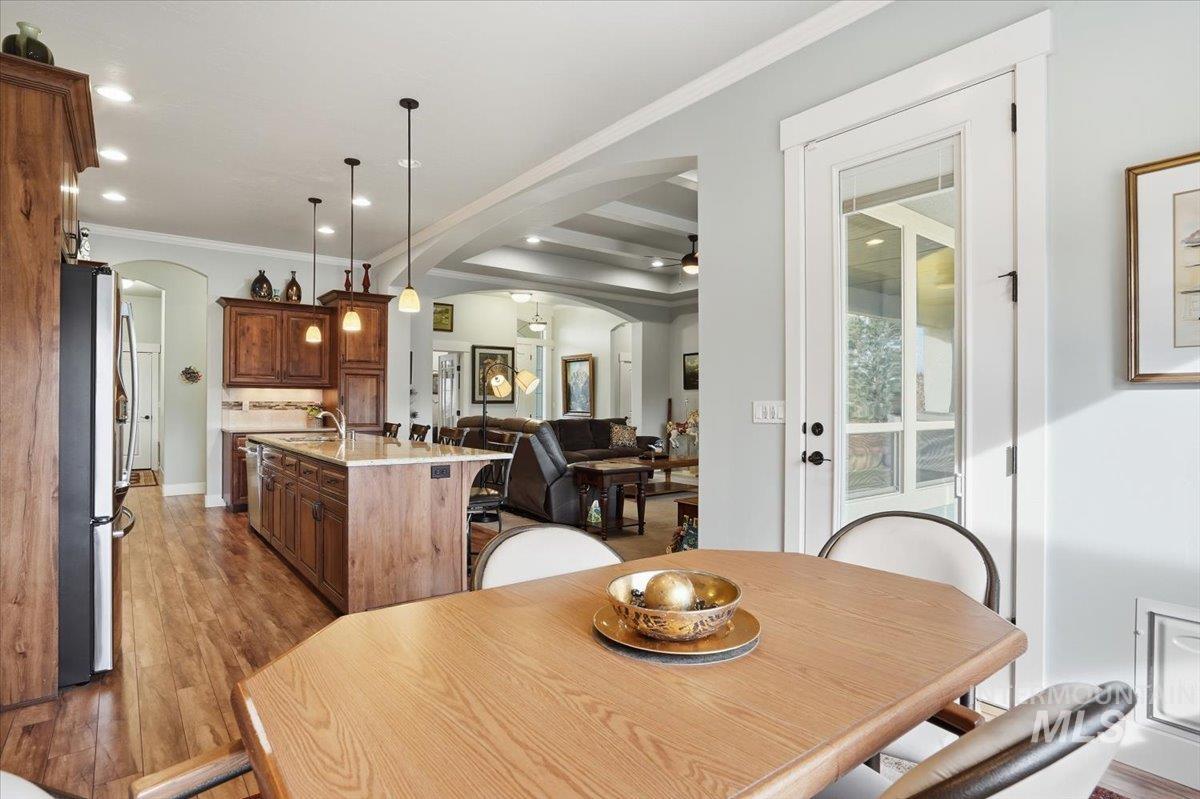 Dining area featuring arched walkways, light wood-type flooring, ornamental molding, recessed lighting, and a raised ceiling