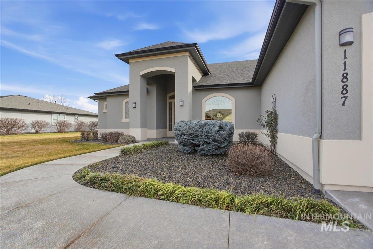 Doorway to property with a yard, stucco siding, and a shingled roof