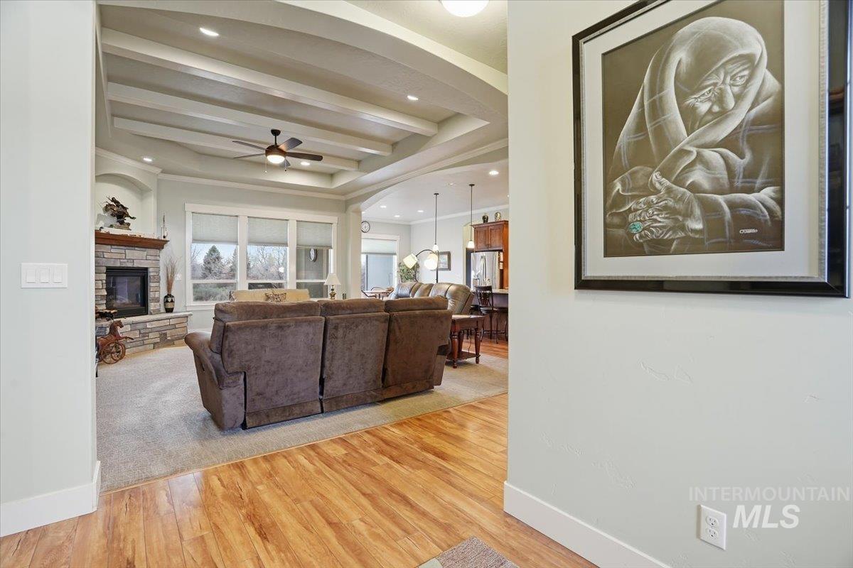 Living area with light wood-type flooring, a fireplace, ceiling fan, recessed lighting, and a tray ceiling