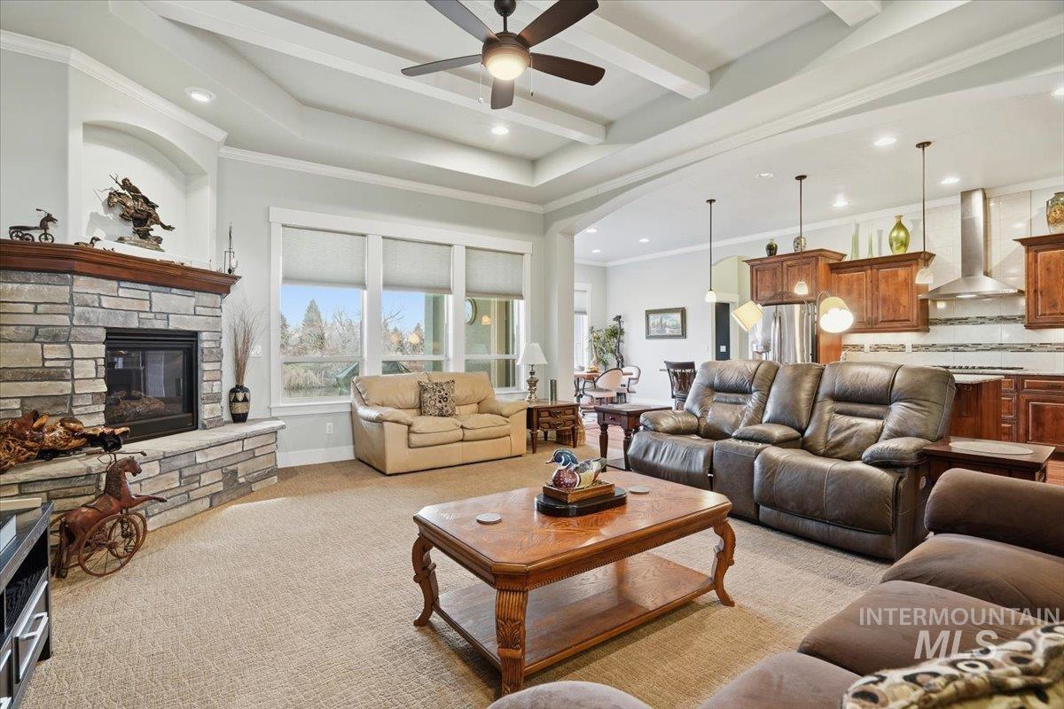 Living room with a ceiling fan, a stone fireplace, light colored carpet, ornamental molding, and recessed lighting
