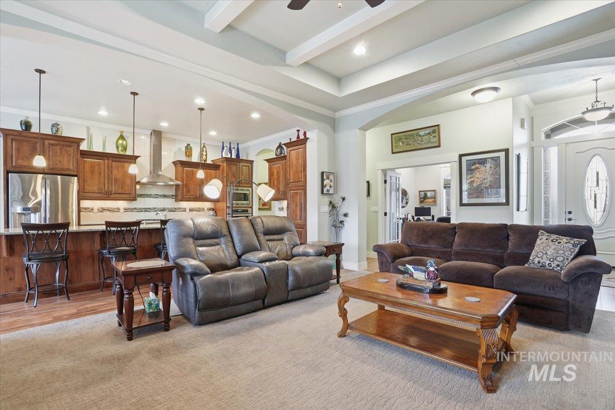 Living room featuring recessed lighting, ceiling fan, crown molding, arched walkways, and beamed ceiling