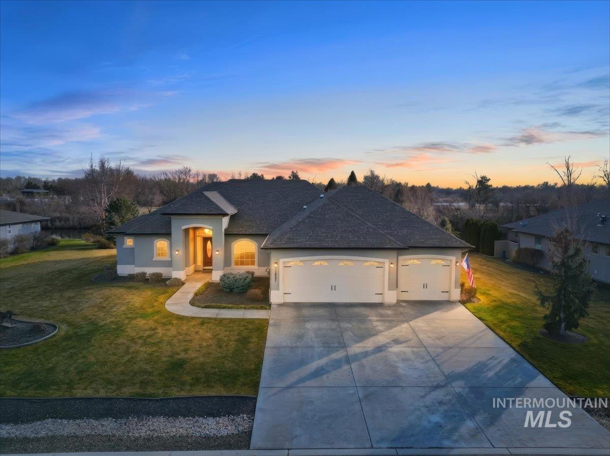 French country inspired facade with a yard, an attached garage, concrete driveway, stucco siding, and roof with shingles