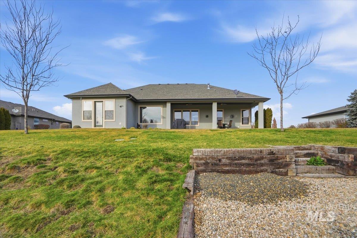 Back of property with stucco siding, a yard, a patio area, and a shingled roof