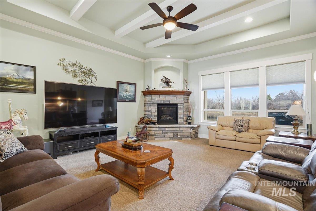 Carpeted living room with a stone fireplace, a ceiling fan, ornamental molding, and recessed lighting