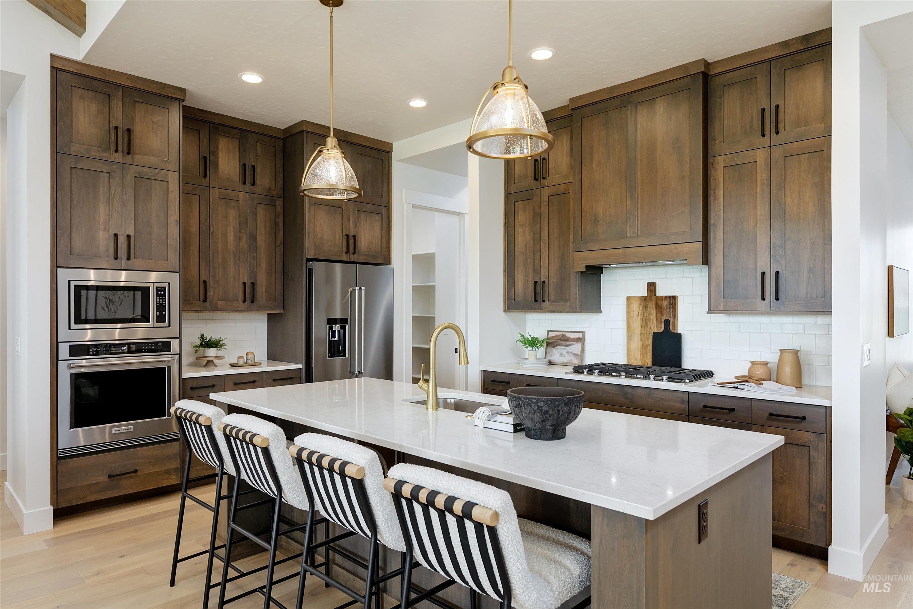 Kitchen featuring tasteful backsplash, a kitchen island with sink, stainless steel appliances, light wood-style floors, and dark wood finish cabinets