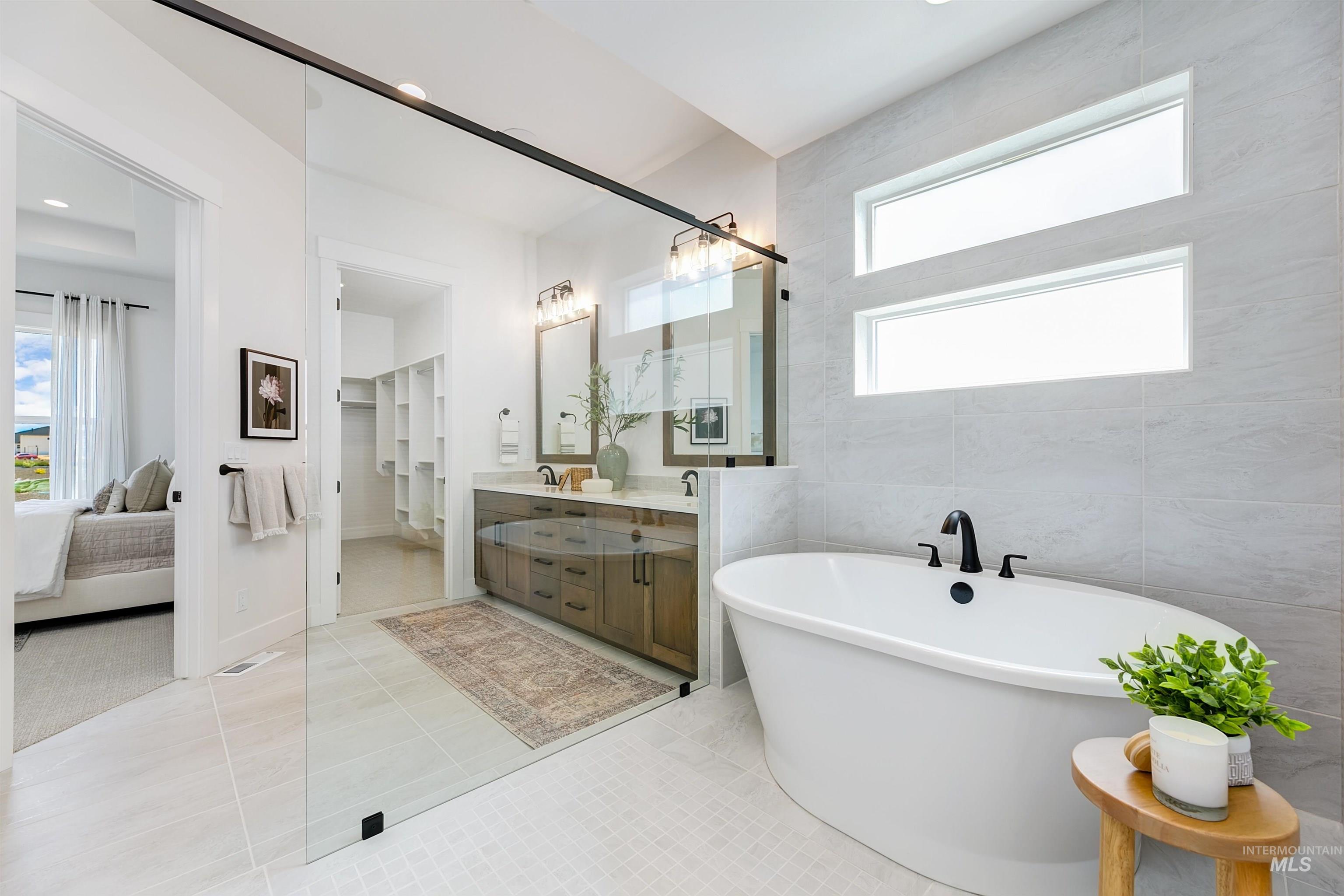 Ensuite bathroom with double vanity, light tile patterned floors, a soaking tub, and tile walls