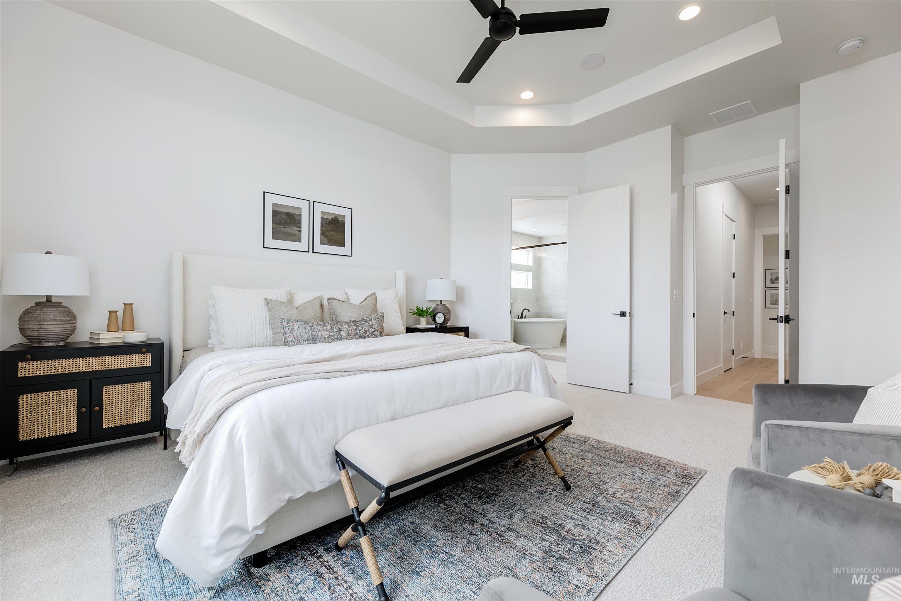 Bedroom with a tray ceiling, light colored carpet, recessed lighting, ceiling fan, and ensuite bathroom