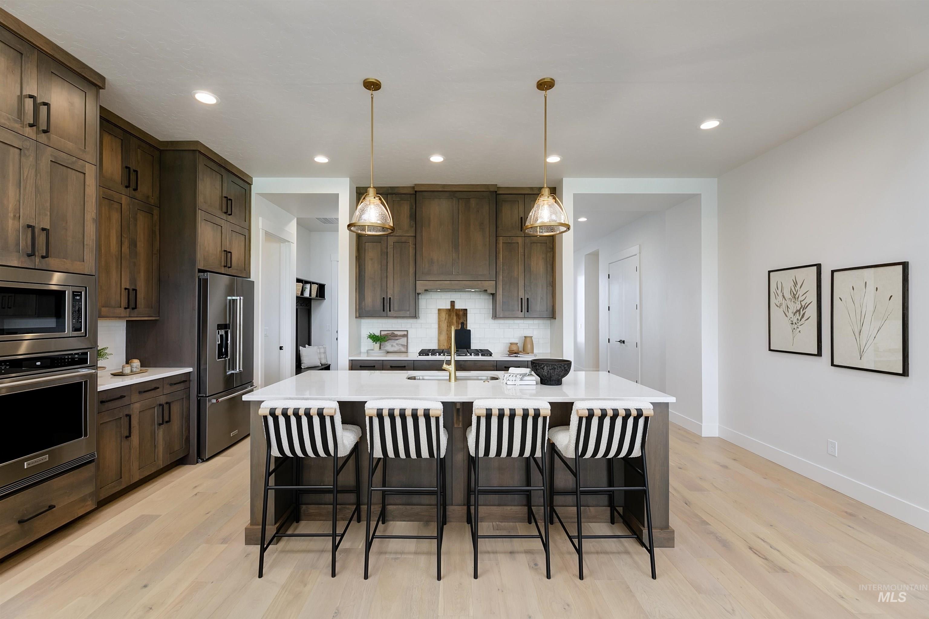 Kitchen featuring dark wood finish cabinetry, a breakfast bar area, stainless steel appliances, a kitchen island with sink, and hanging light fixtures