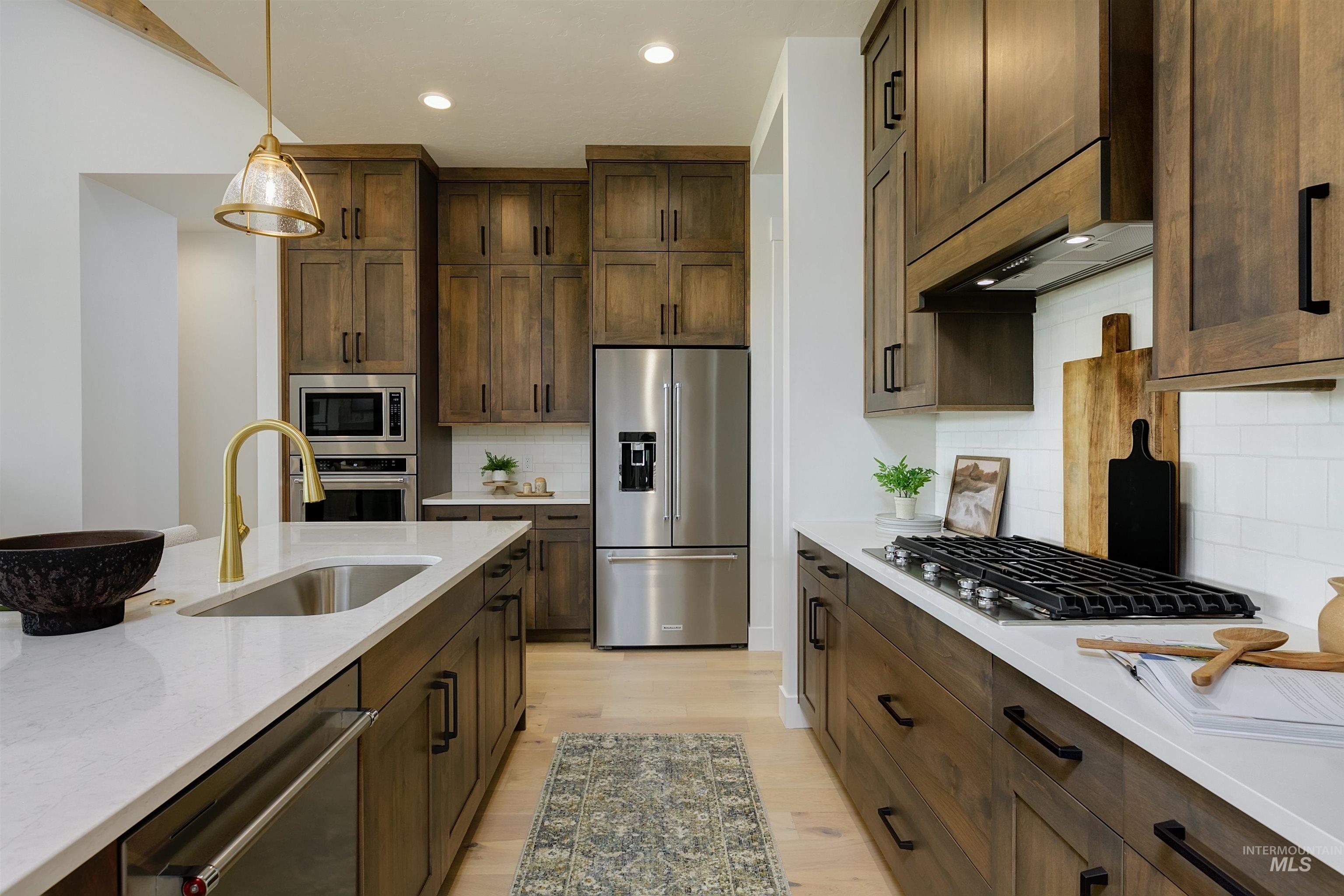 Kitchen with stainless steel appliances, light wood finished floors, light stone counters, pendant lighting, and decorative backsplash