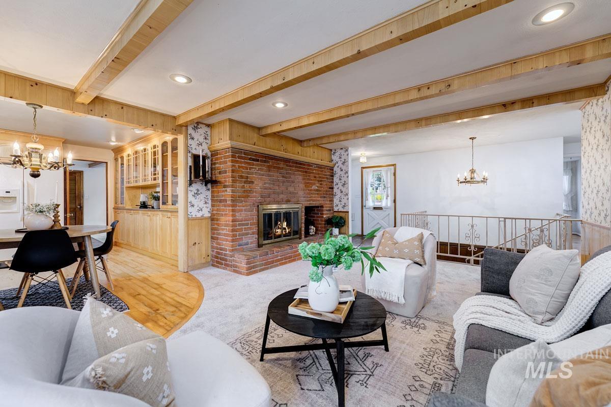 Living room with a chandelier, beam ceiling, a fireplace, a wainscoted wall, and wooden walls