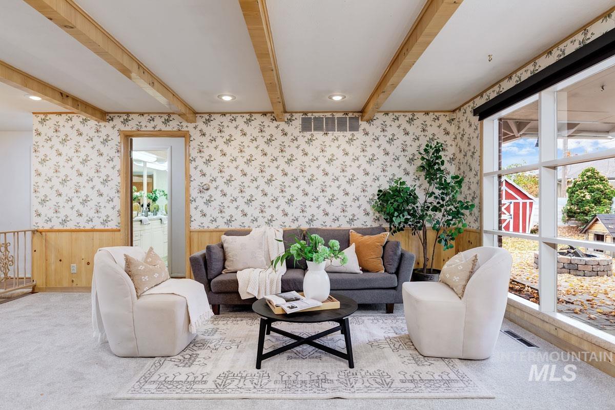 Living area featuring wallpapered walls, beam ceiling, carpet, wainscoting, and wooden walls