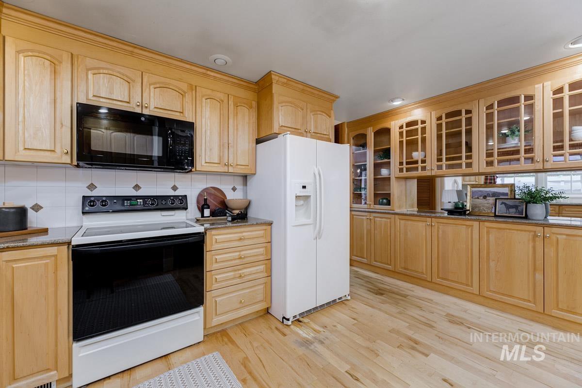 Kitchen featuring white appliances, light brown cabinets, glass insert cabinets, and recessed lighting