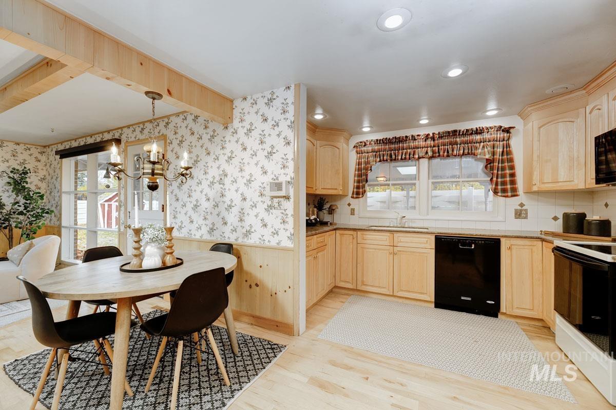 Kitchen featuring wainscoting, light brown cabinetry, black appliances, light wood finished floors, and a chandelier