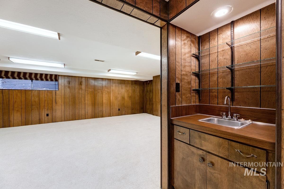 Bar with wooden walls, carpet flooring, open shelves, and brown cabinetry