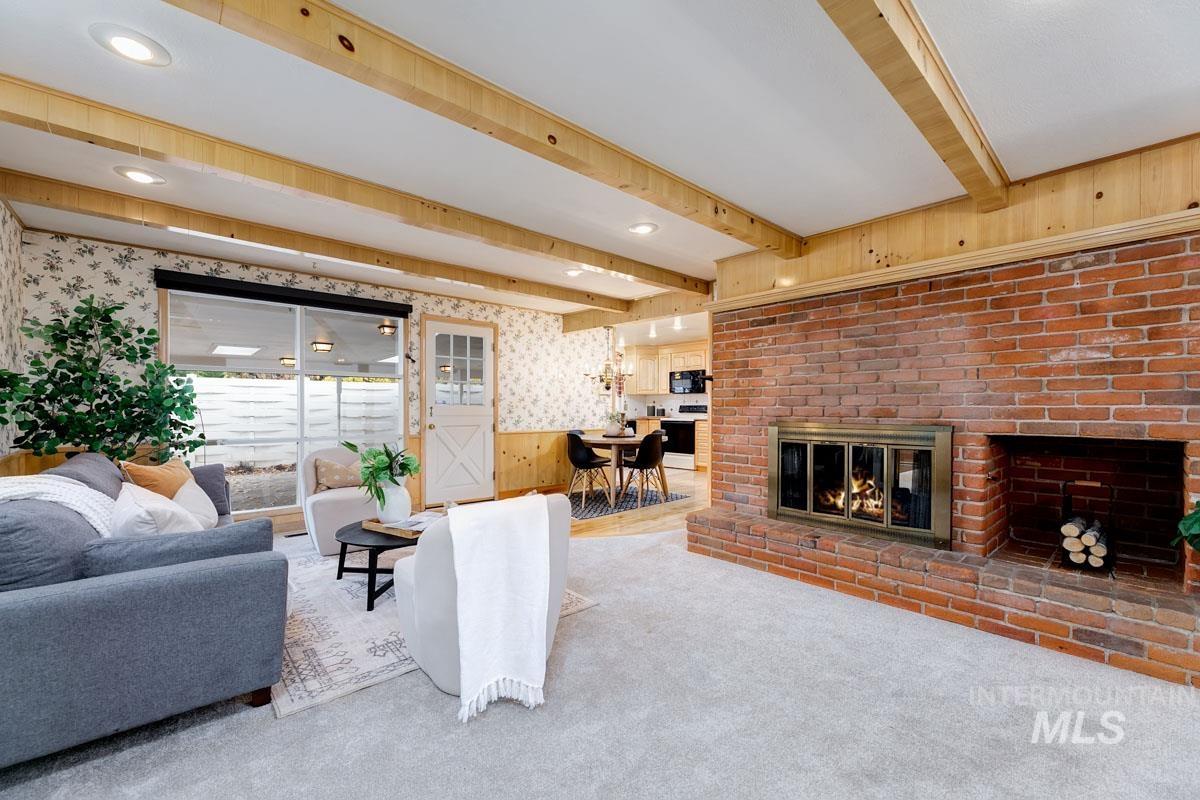 Carpeted living area with wallpapered walls, a wainscoted wall, a fireplace, beam ceiling, and wooden walls