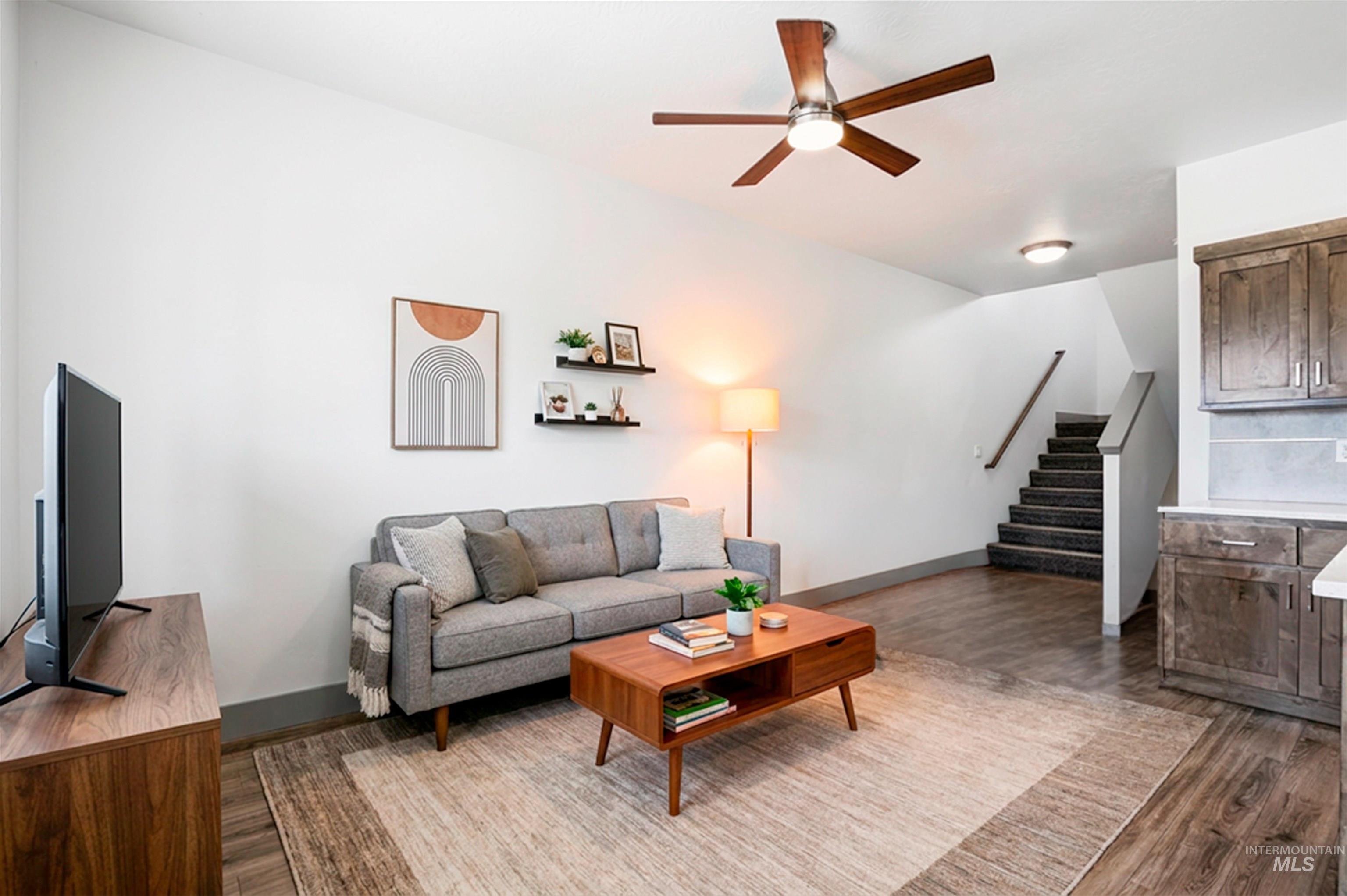 Open-concept living area with wood-finish flooring, a contemporary ceiling fan, and a staircase featuring carpeted treads and a wooden handrail