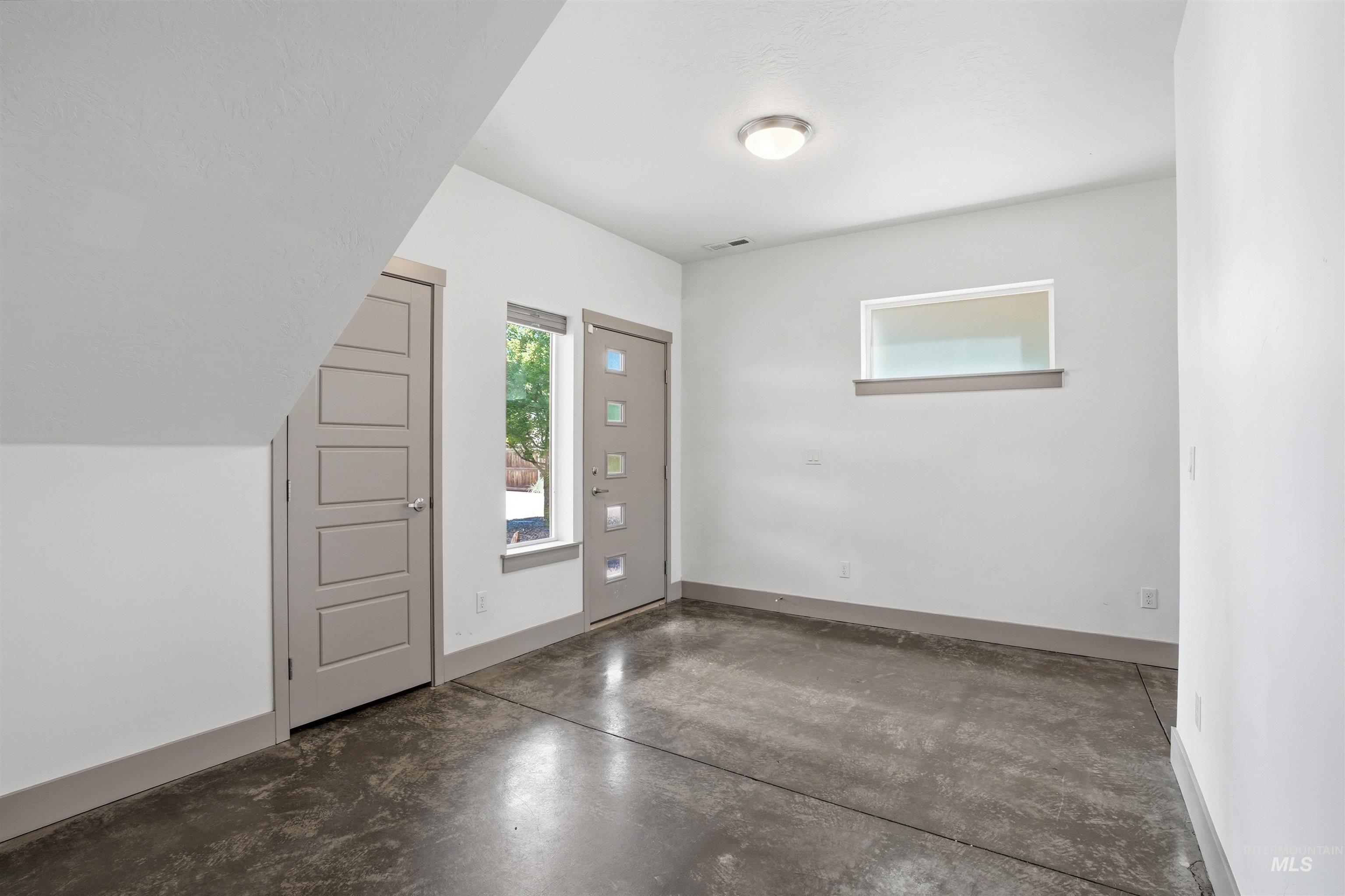 Concrete flooring with a matte finish, modern grey paneled doors, and contemporary windows