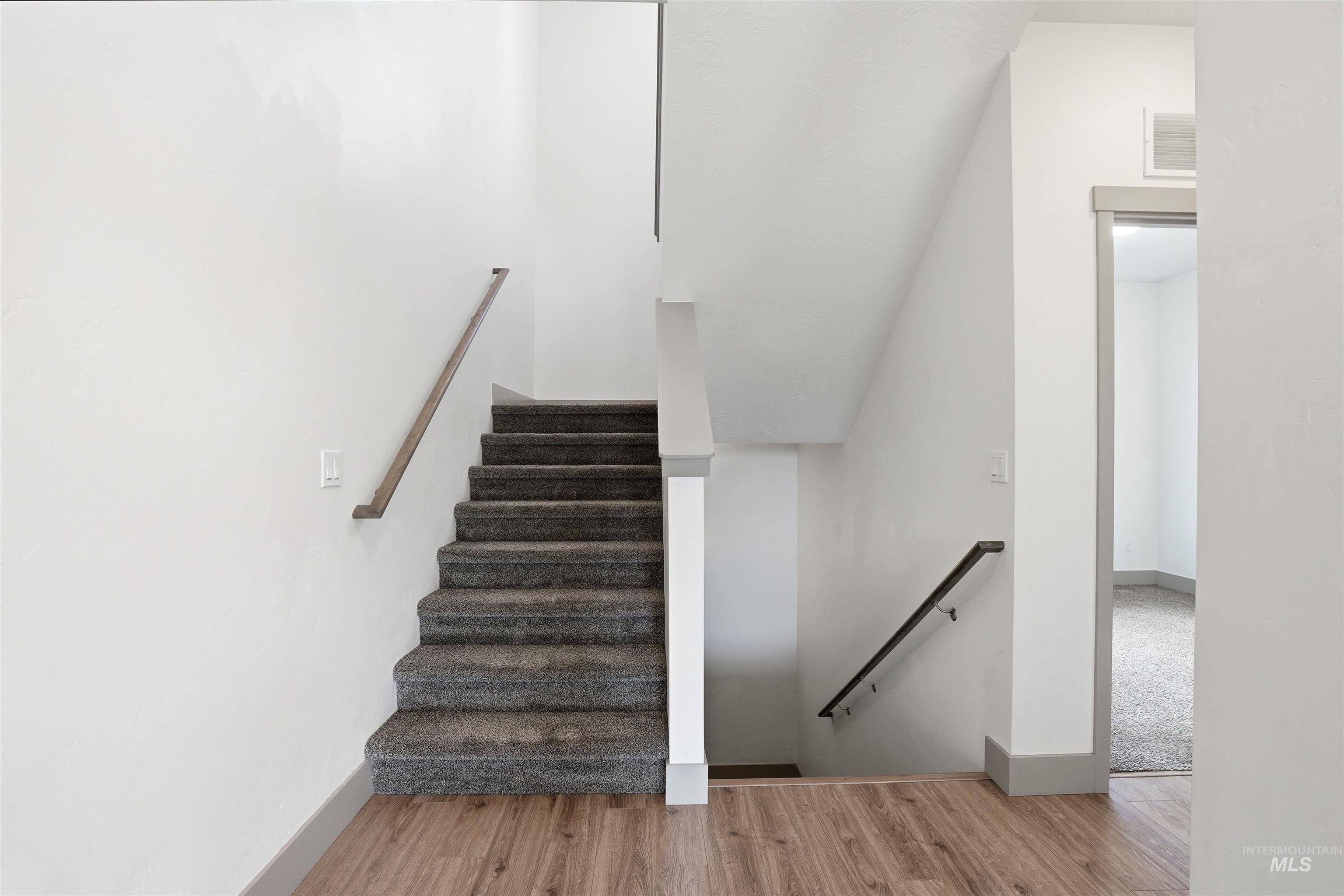 Carpeted staircase with wood-finish handrails, crisp white walls, and durable wood-finish flooring extending into the entryway