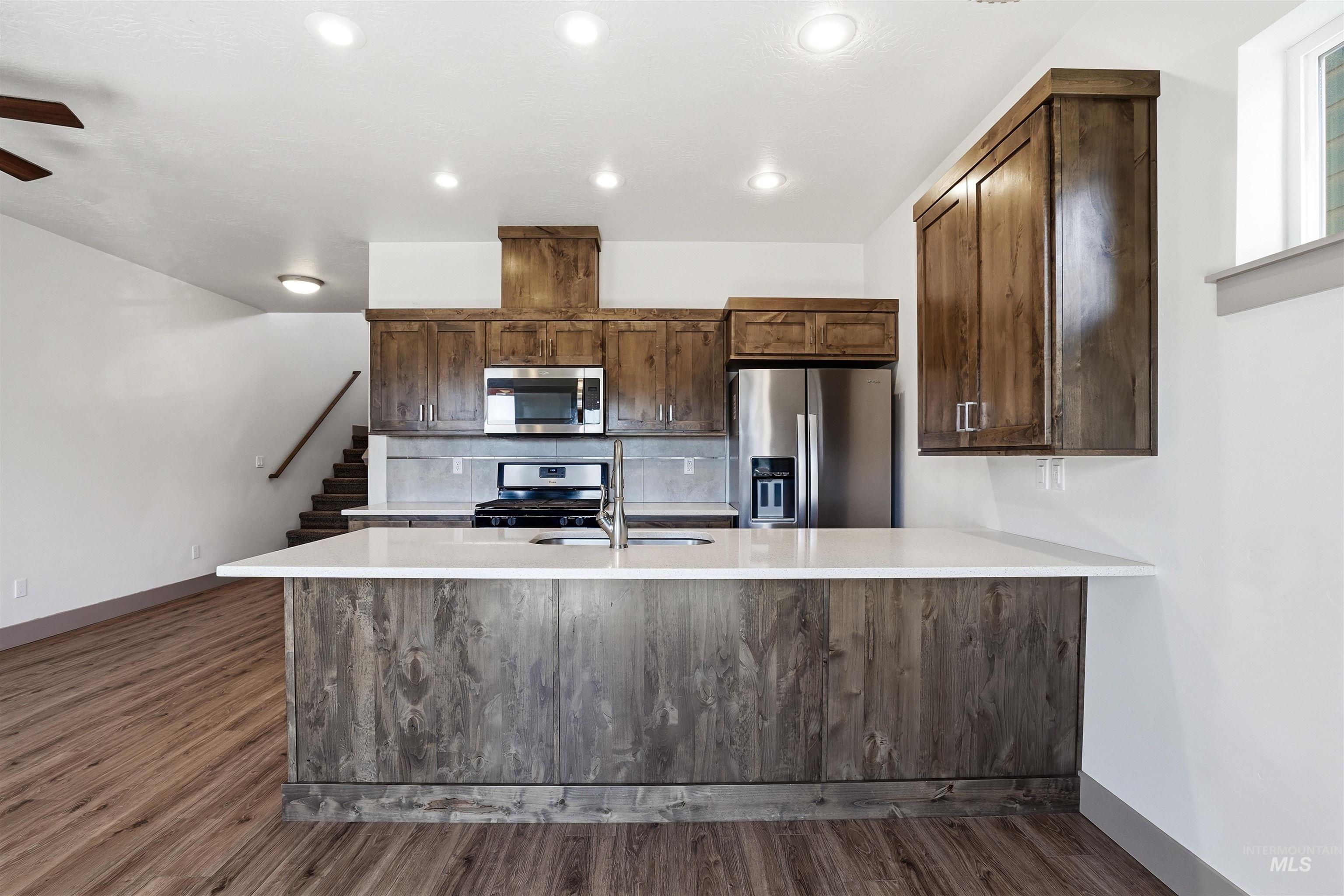Kitchen featuring a spacious island with a light-toned countertop, stainless steel appliances, wood-finish cabinetry, and recessed lighting