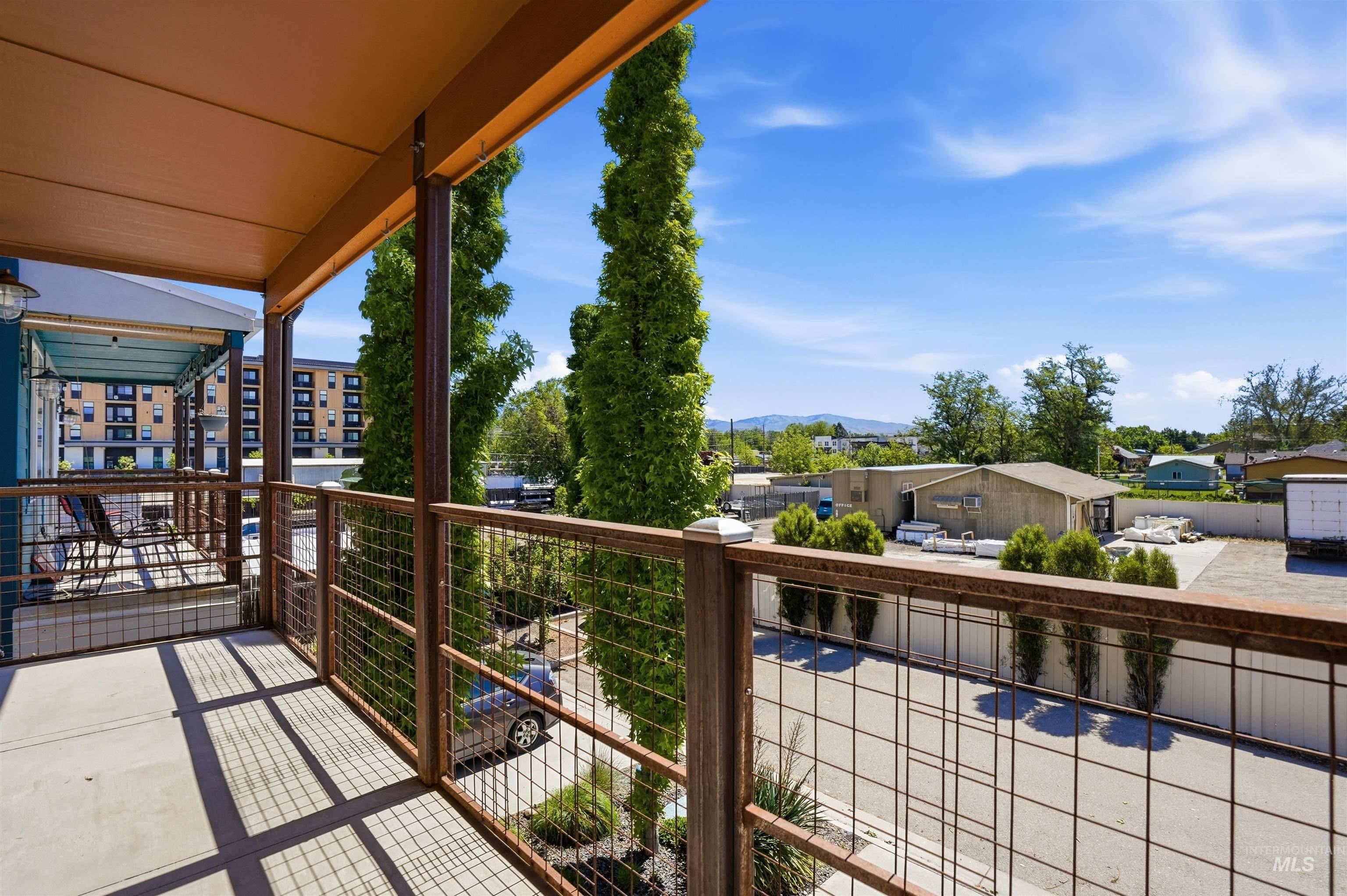 Spacious outdoor balcony featuring durable concrete flooring, metal railing with mesh infill, and a covered ceiling