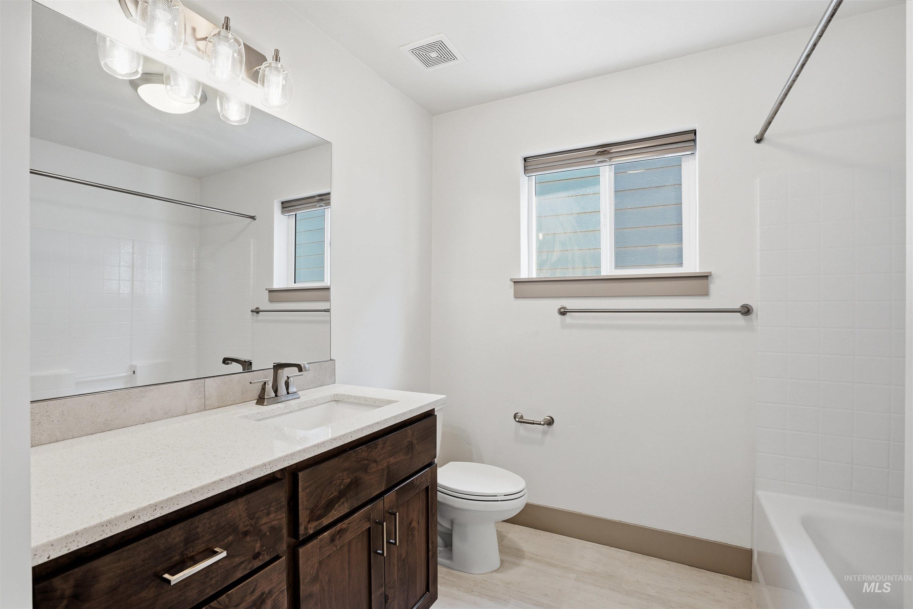 Contemporary bathroom featuring a dark wood-finish vanity with a light-toned countertop, an integrated sink, and brushed nickel fixtures