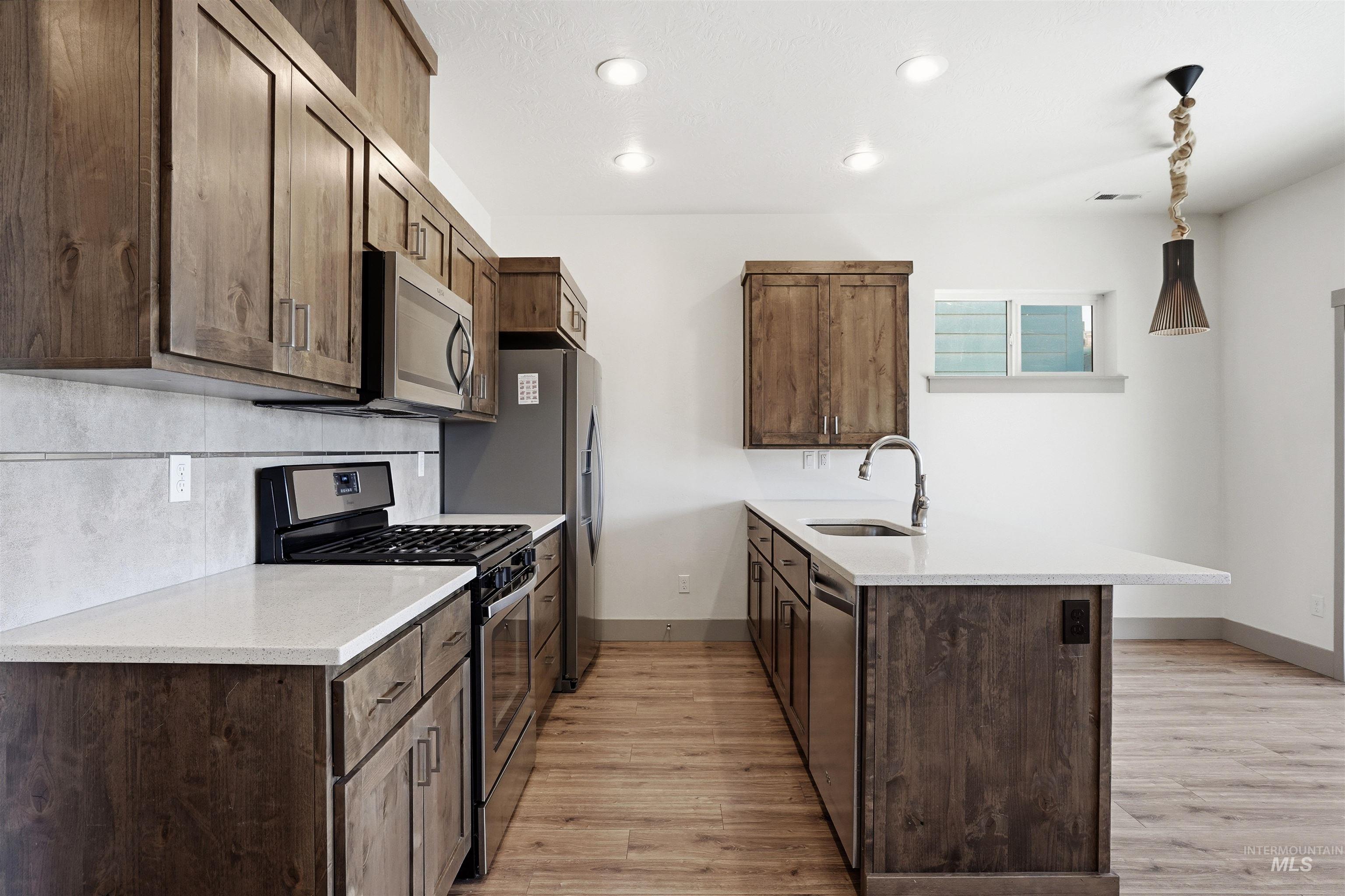 Kitchen featuring wood-finish cabinetry, light-toned countertops, and stainless steel appliances