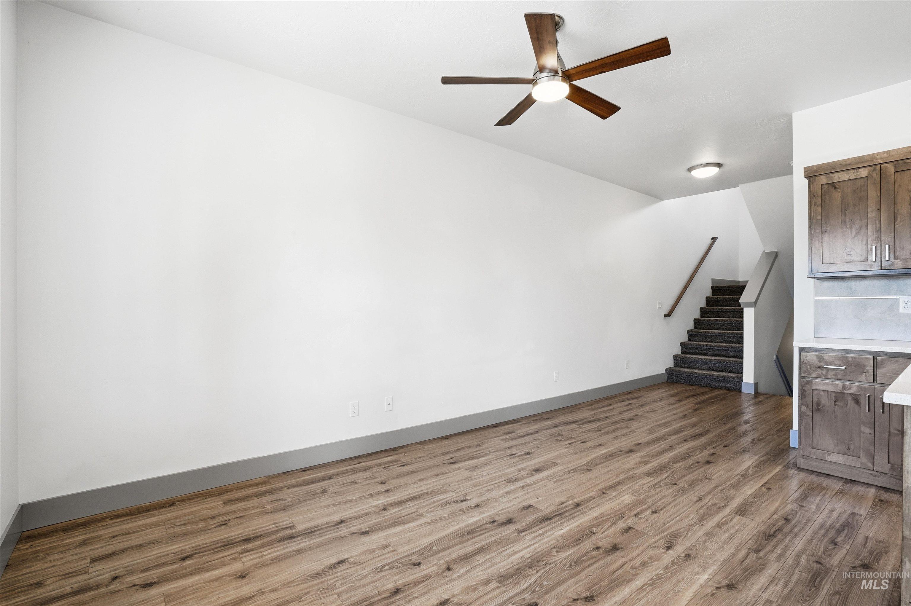 Spacious interior featuring wood-finish flooring, a modern ceiling fan with integrated lighting, and a staircase with a wood handrail