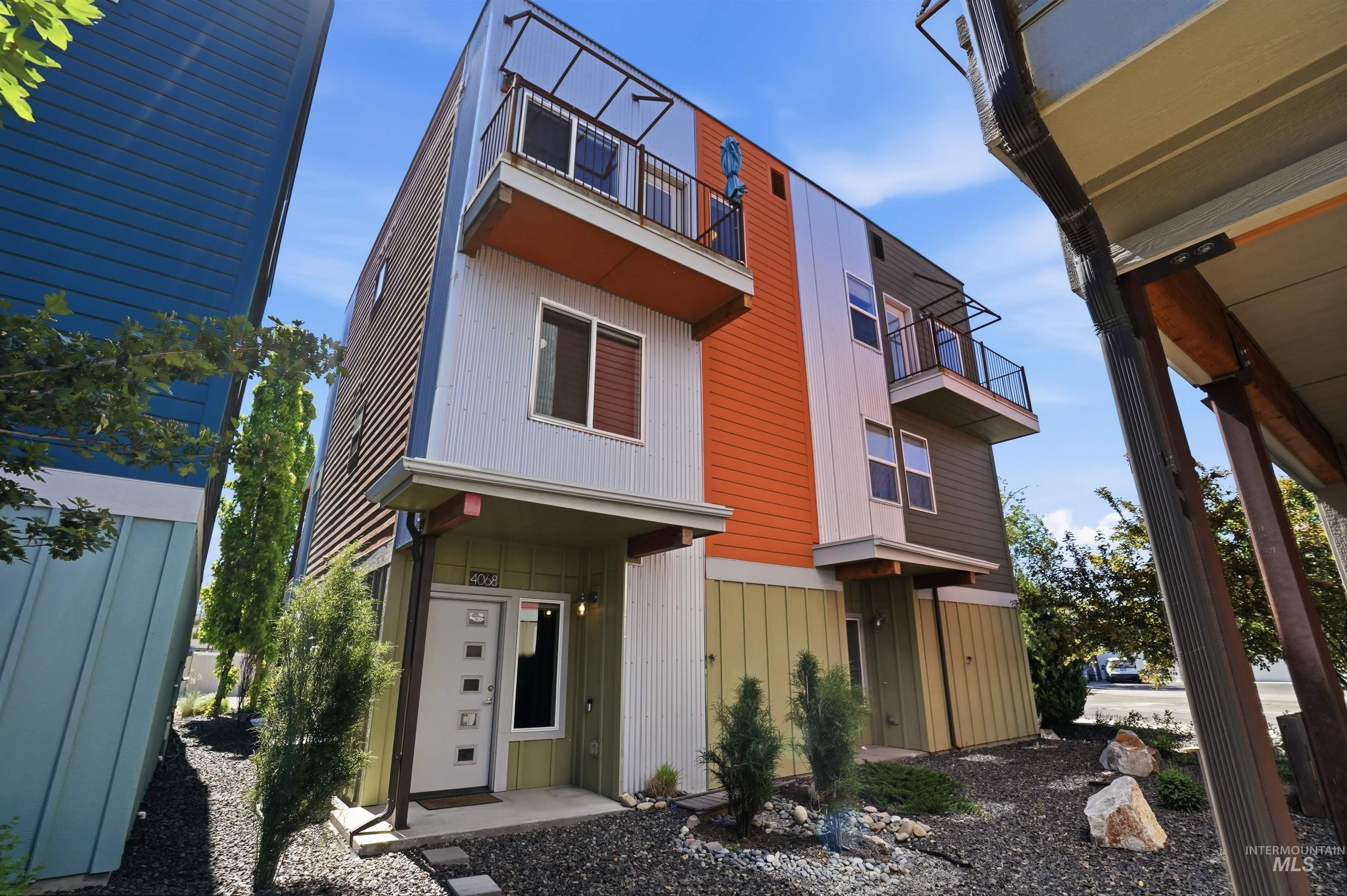 Modern multi-story exterior featuring corrugated metal siding, distinct color-block panels, and multiple private balconies with metal railings