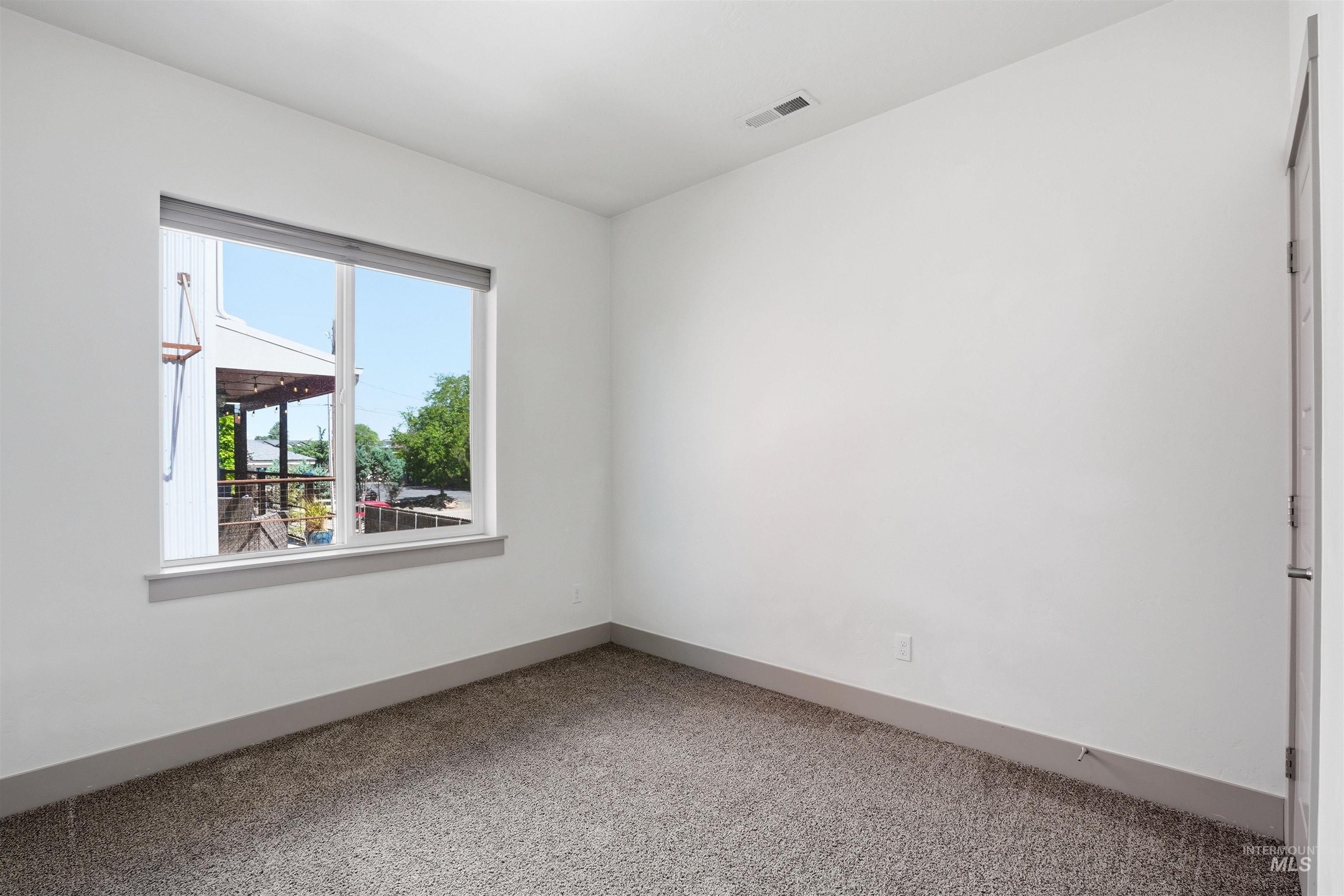 Bright interior space featuring a large window, neutral carpeting, white walls, and a gray baseboard trim