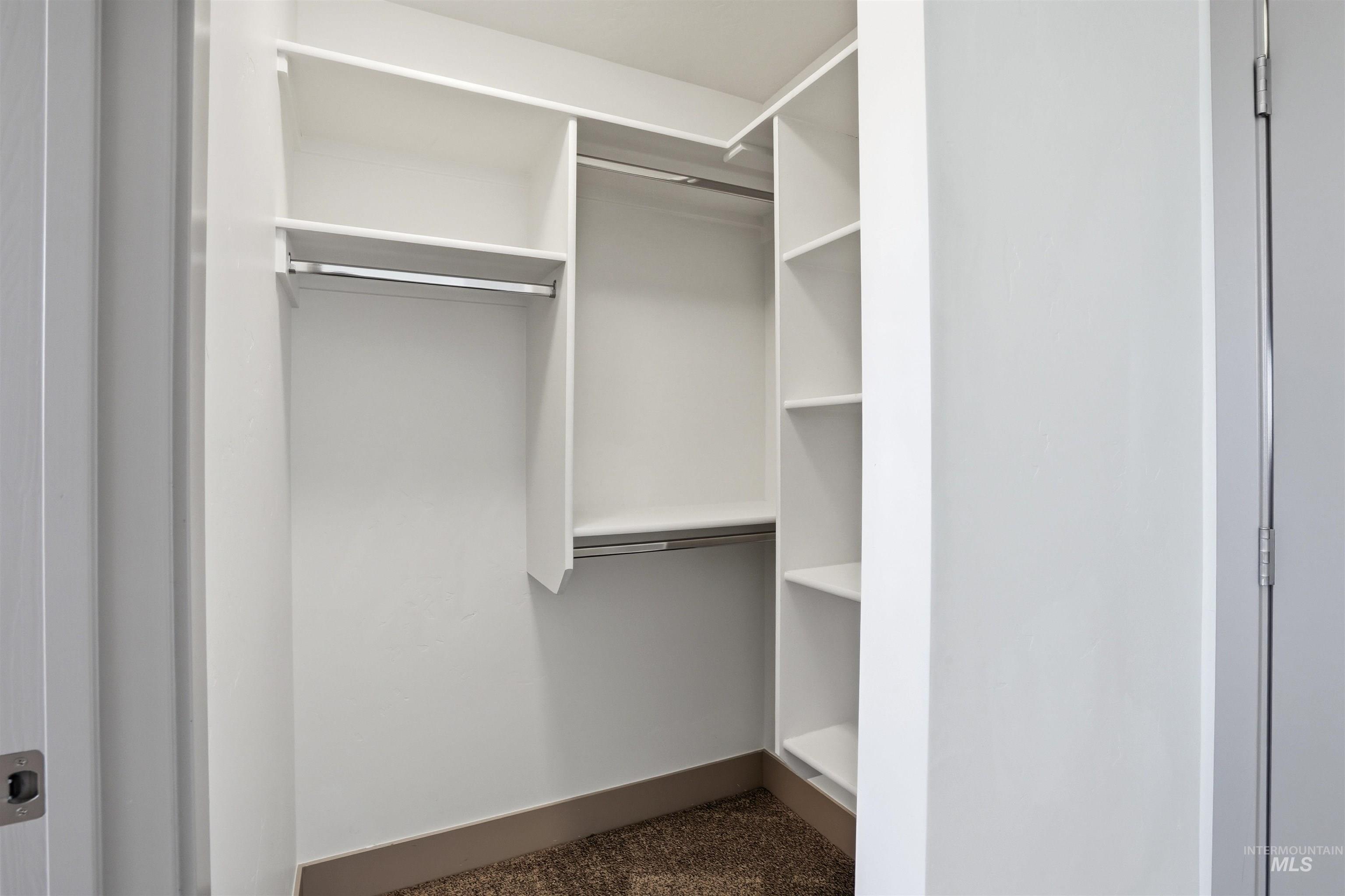 Built-in closet system featuring white shelving, multiple hanging rods, and a neutral carpet floor