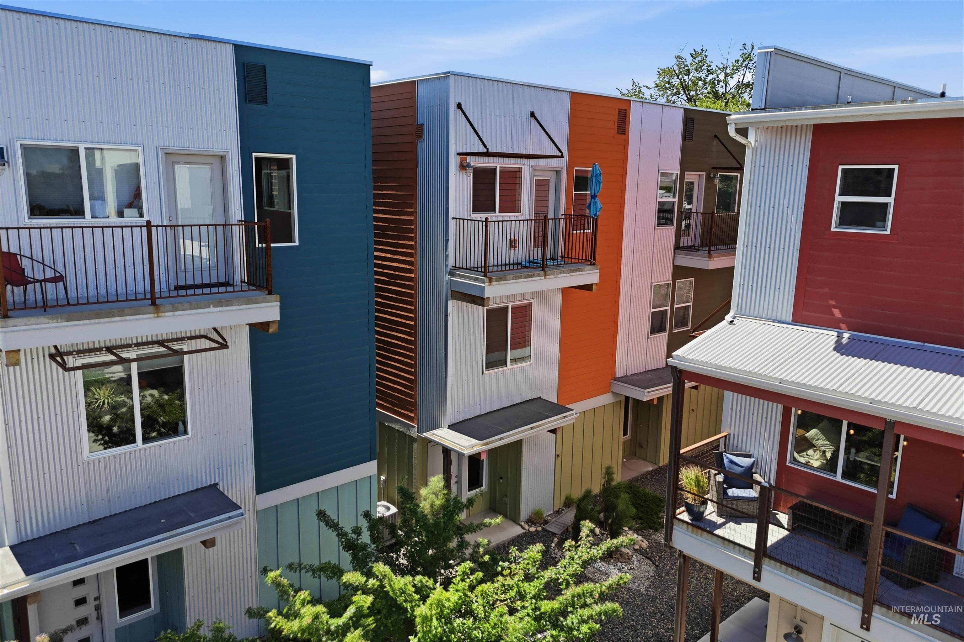 Multi-level residences featuring corrugated metal siding, various color-blocked facades, individual balconies with metal railings, and ground-level patios