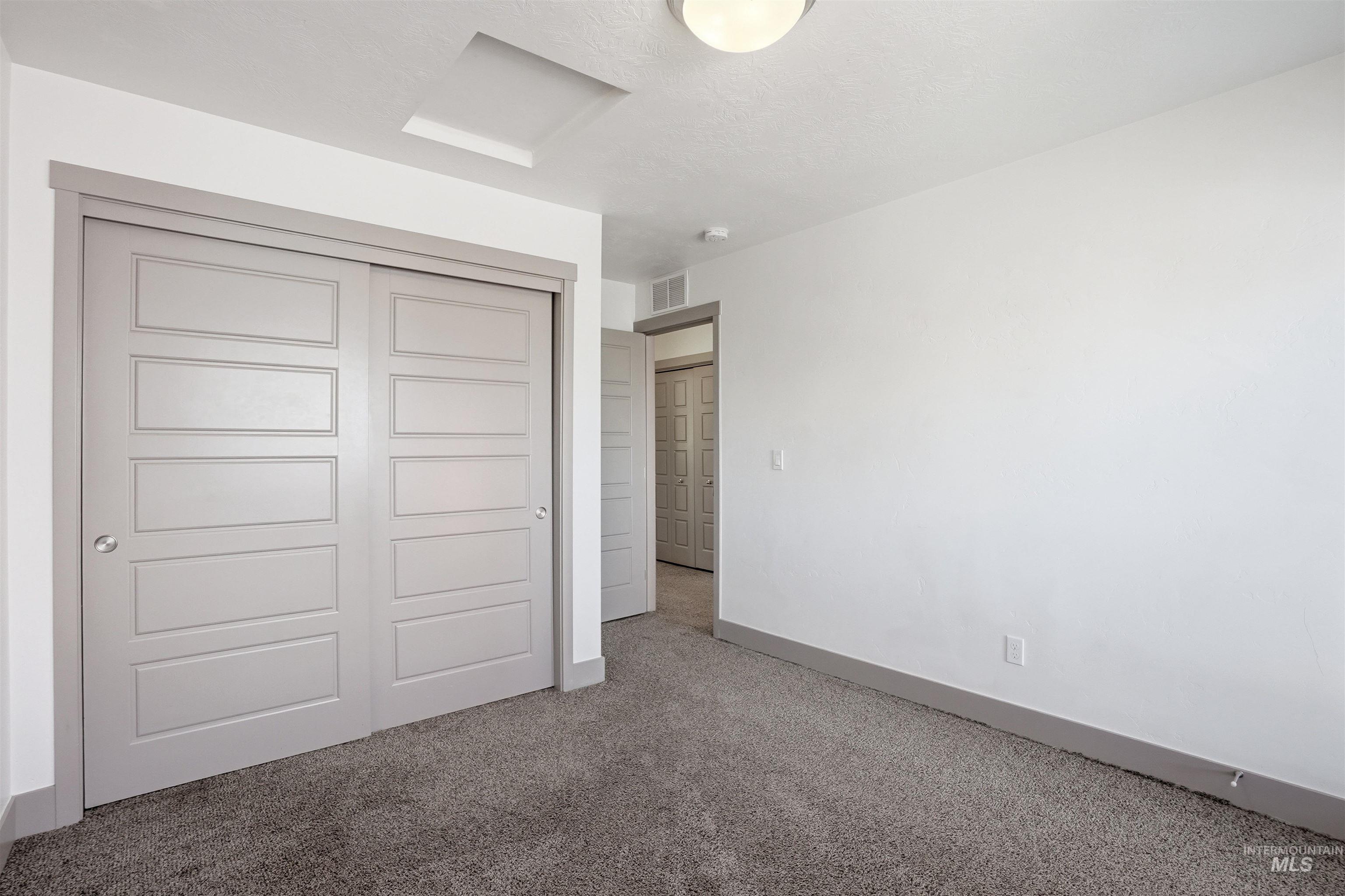 Interior room featuring grey panel sliding closet doors, grey baseboards, and grey carpet flooring