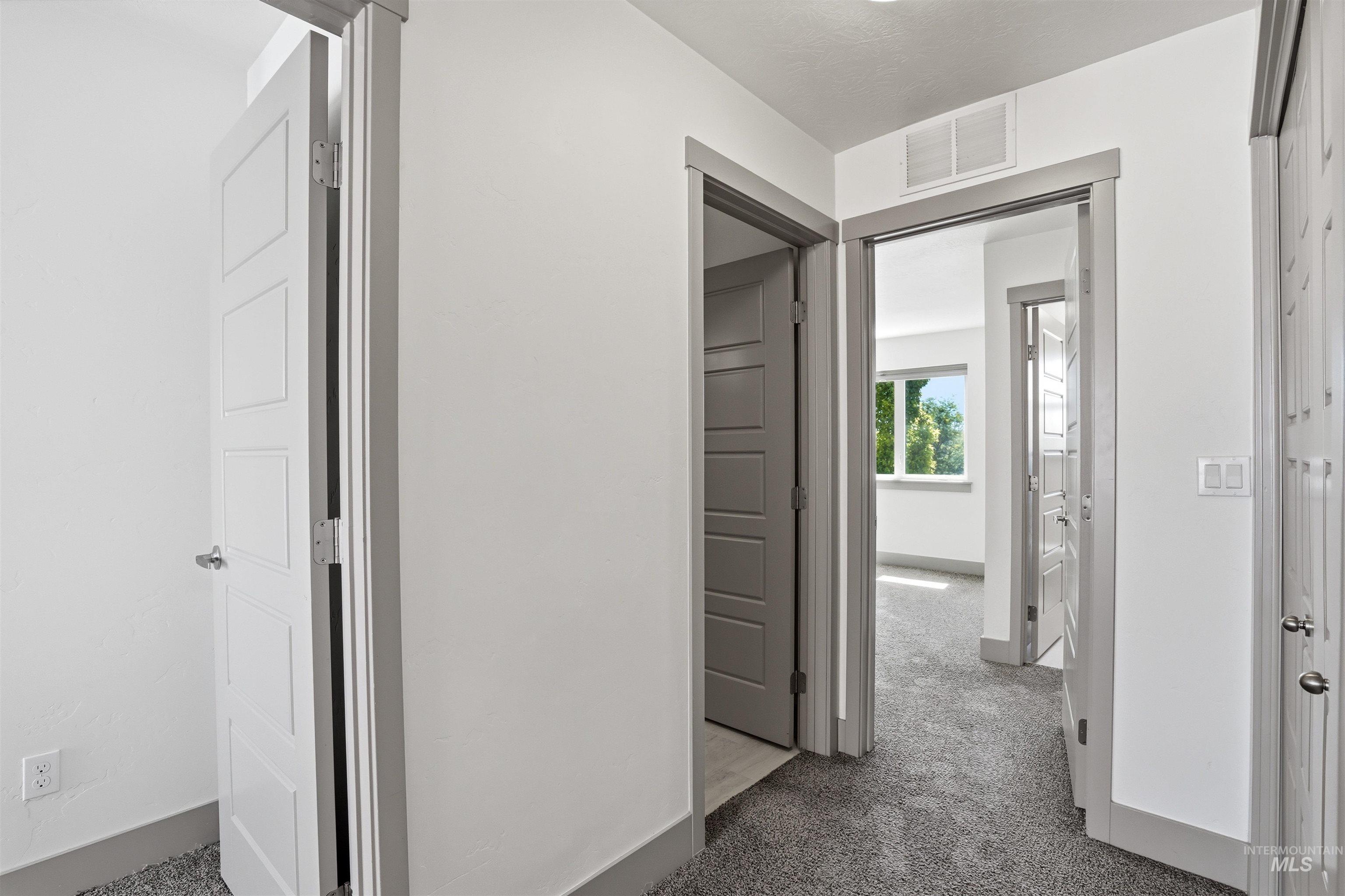 Hallway featuring durable gray carpeting, white walls, and contemporary panel doors with coordinating gray trim